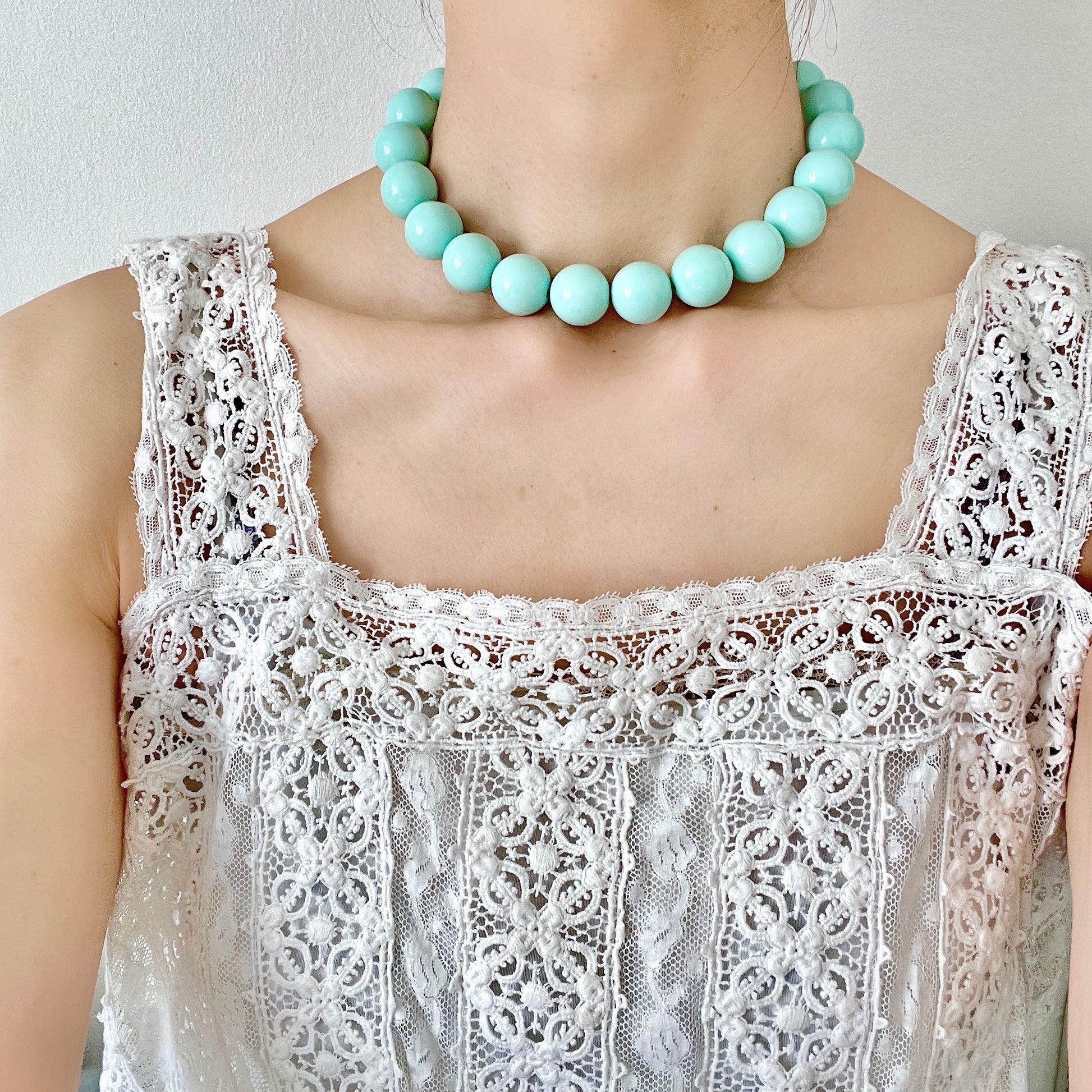 A choker necklace with large ice blue plastic beads, adding a subtle pop of cool color around the neck.  さわやかなアイスブルーのプラスチックビーズ のチョーカーネックレス。
