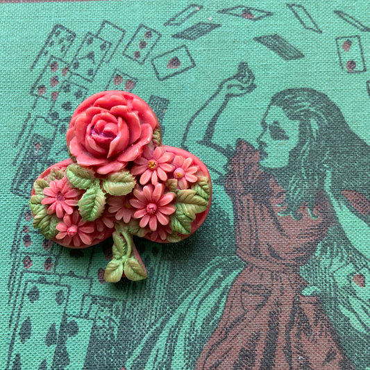 A brooch featuring a three-leaf clover motif, adorned with red roses and daisy flowers shaped into the design. 三つ葉クローバーのモチーフに、赤いバラやデイジーのお花が象られたブローチ。
