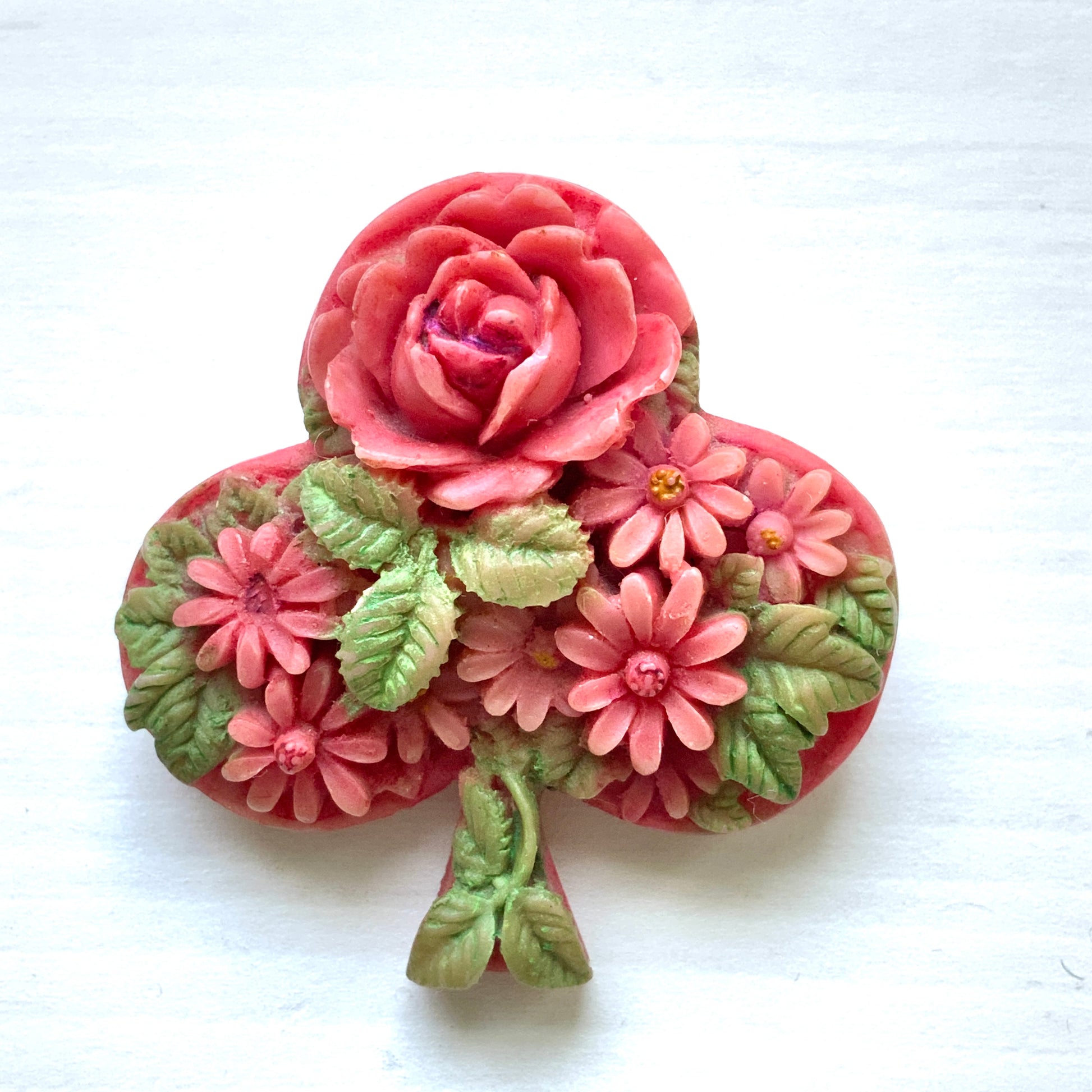 A brooch featuring a three-leaf clover motif, adorned with red roses and daisy flowers shaped into the design. 三つ葉クローバーのモチーフに、赤いバラやデイジーのお花が象られたブローチ。
