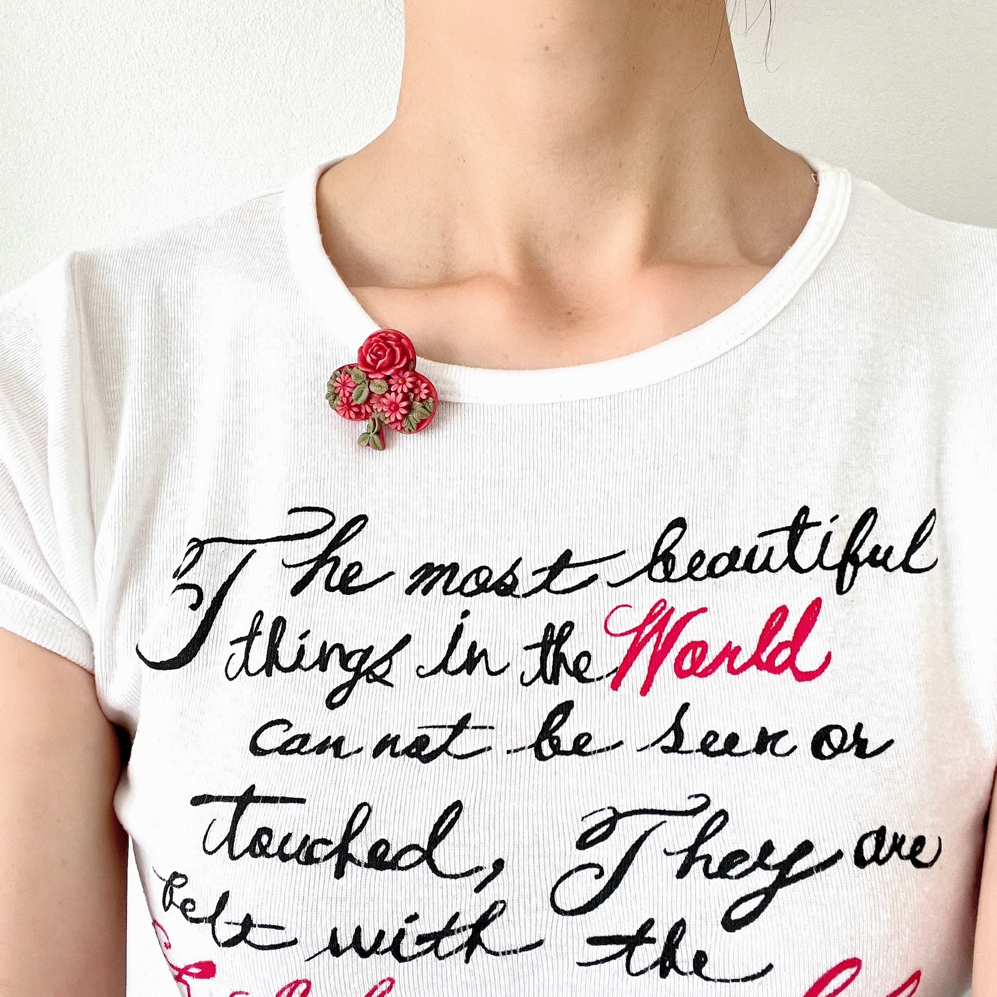 A brooch featuring a three-leaf clover motif, adorned with red roses and daisy flowers shaped into the design. 三つ葉クローバーのモチーフに、赤いバラやデイジーのお花が象られたブローチ。
