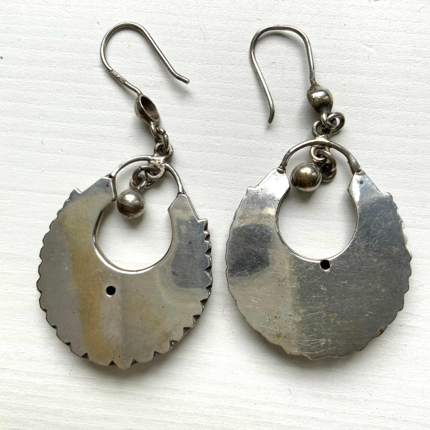 Striking silver tone hoop earrings with geometric embossed patterns and granulated bead details. 半月型にジオメトリックな打ち出し模様と粒状の装飾を施した、存在感あるシルバートーンのフープピアス。