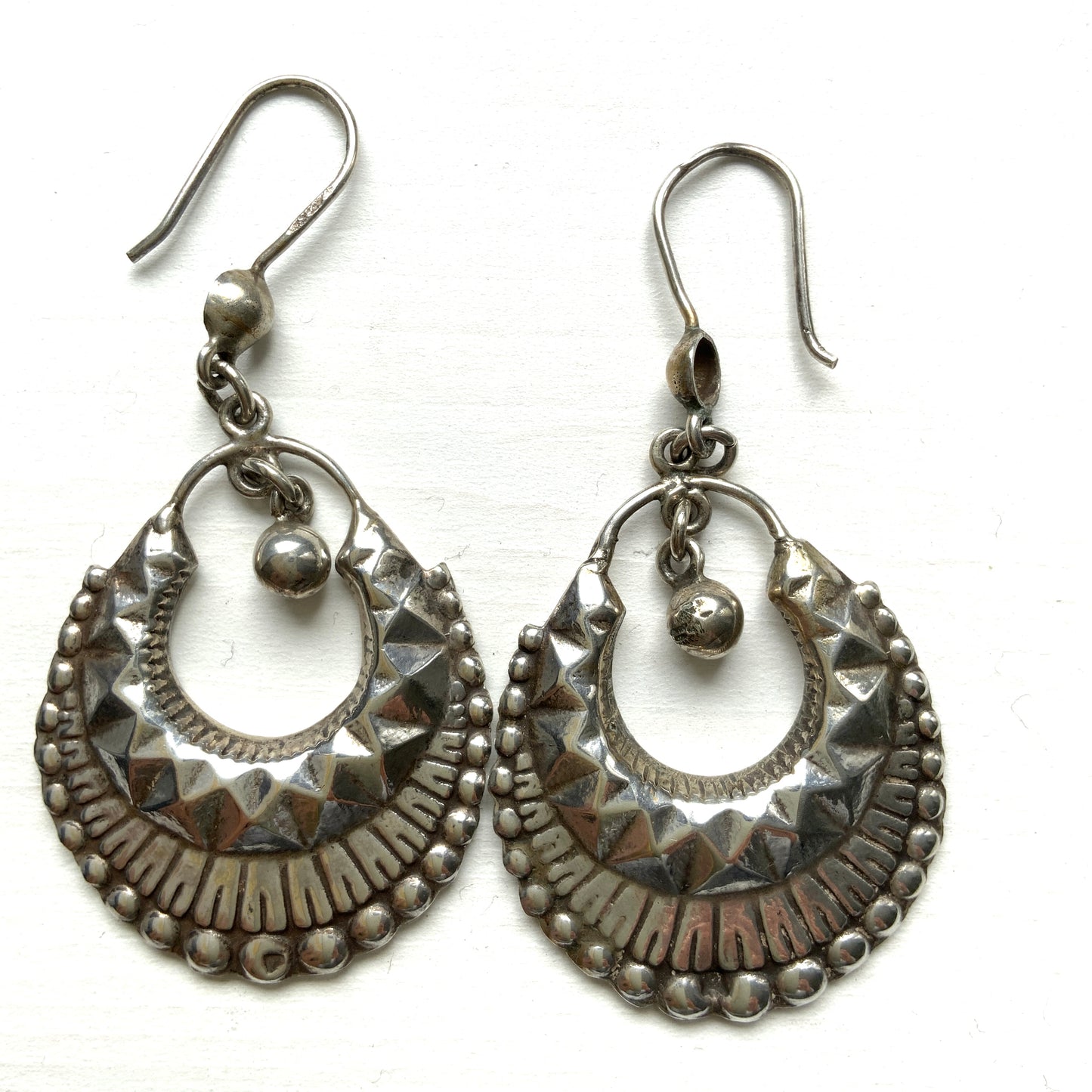 Striking silver tone hoop earrings with geometric embossed patterns and granulated bead details. 半月型にジオメトリックな打ち出し模様と粒状の装飾を施した、存在感あるシルバートーンのフープピアス。