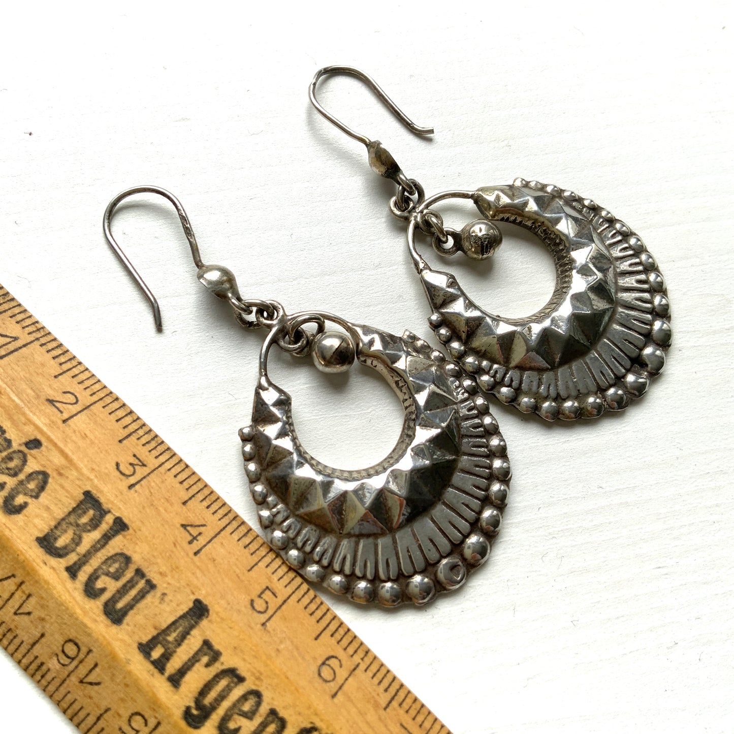 Striking silver tone hoop earrings with geometric embossed patterns and granulated bead details. 半月型にジオメトリックな打ち出し模様と粒状の装飾を施した、存在感あるシルバートーンのフープピアス。
