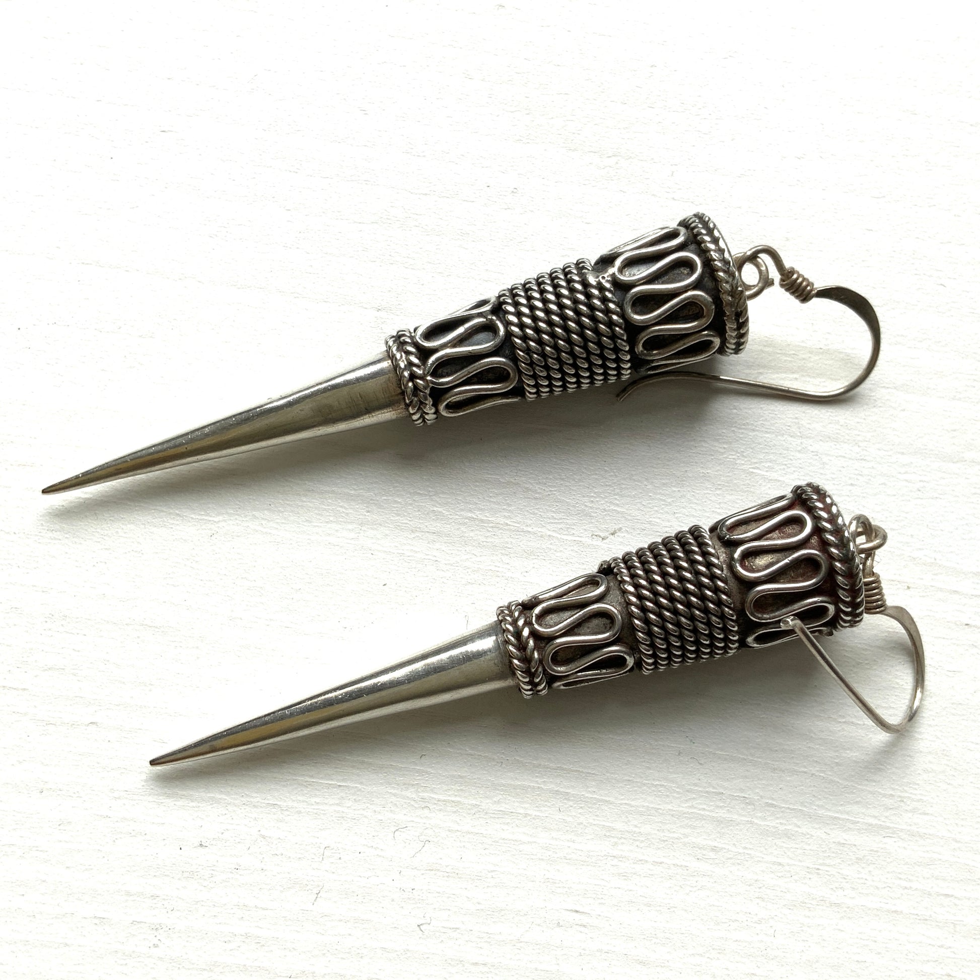 Silver spike-shaped earrings with tribal-inspired patterns.  トライバルな模様が入った細長いスパイク型のシルバーピアス。