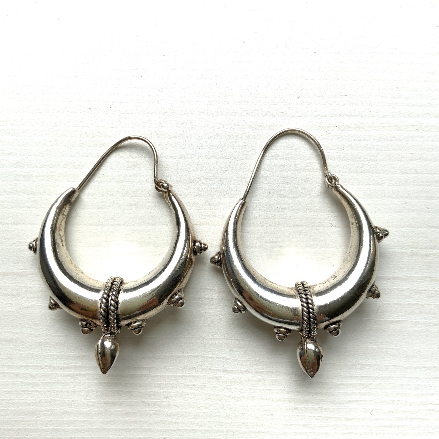 Bold silver hoop earrings in a crescent form, decorated with granulated details and teardrop-shaped protrusions. 三日月型に粒状の装飾とドロップ状の突起をあしらった存在感のあるシルバーフープピアス。