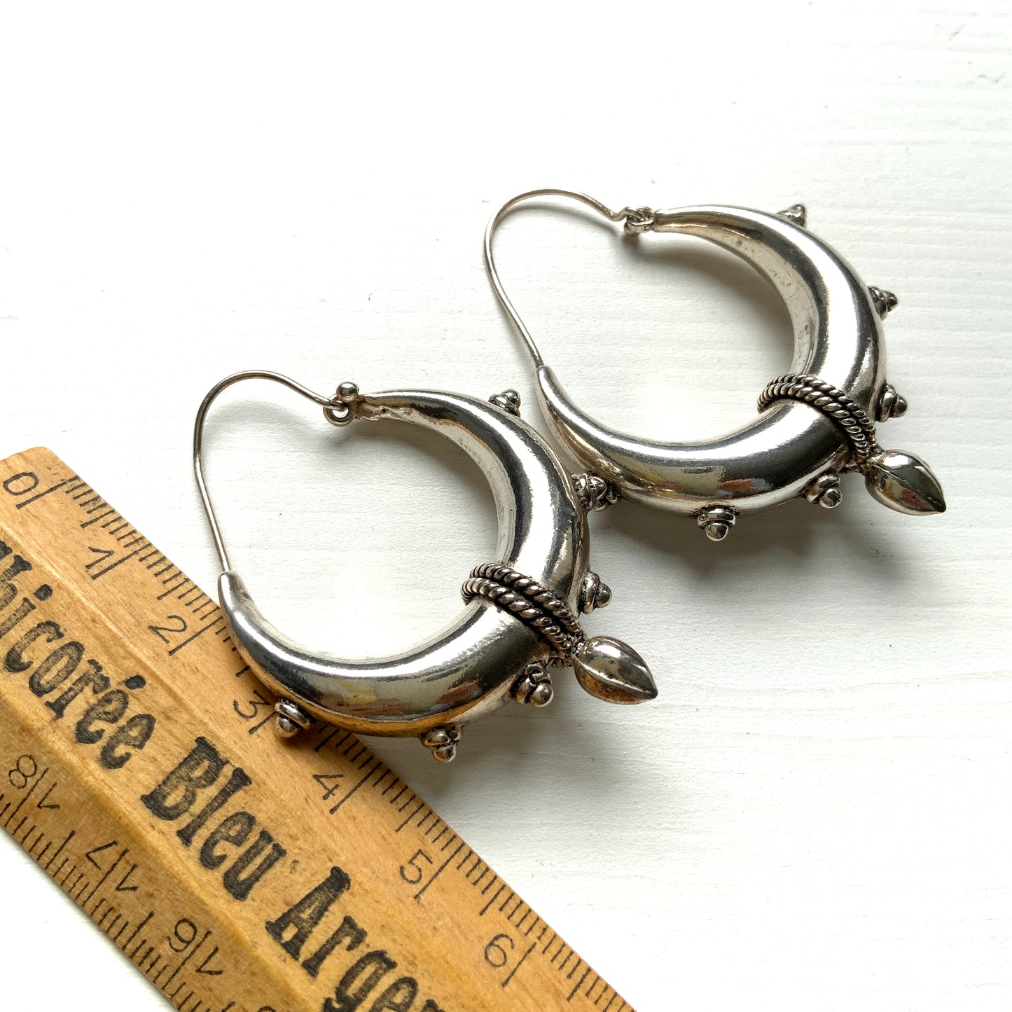Bold silver hoop earrings in a crescent form, decorated with granulated details and teardrop-shaped protrusions. 三日月型に粒状の装飾とドロップ状の突起をあしらった存在感のあるシルバーフープピアス。