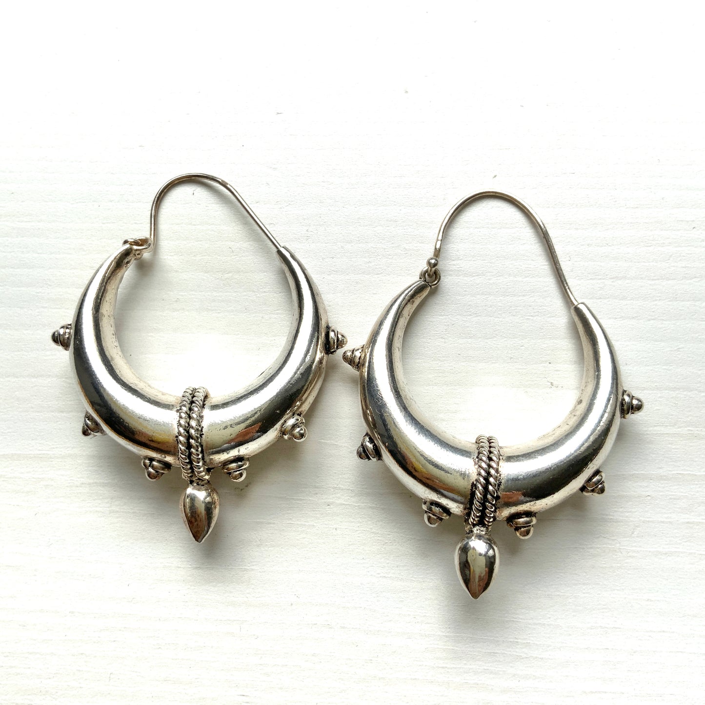 Bold silver hoop earrings in a crescent form, decorated with granulated details and teardrop-shaped protrusions. 三日月型に粒状の装飾とドロップ状の突起をあしらった存在感のあるシルバーフープピアス。
