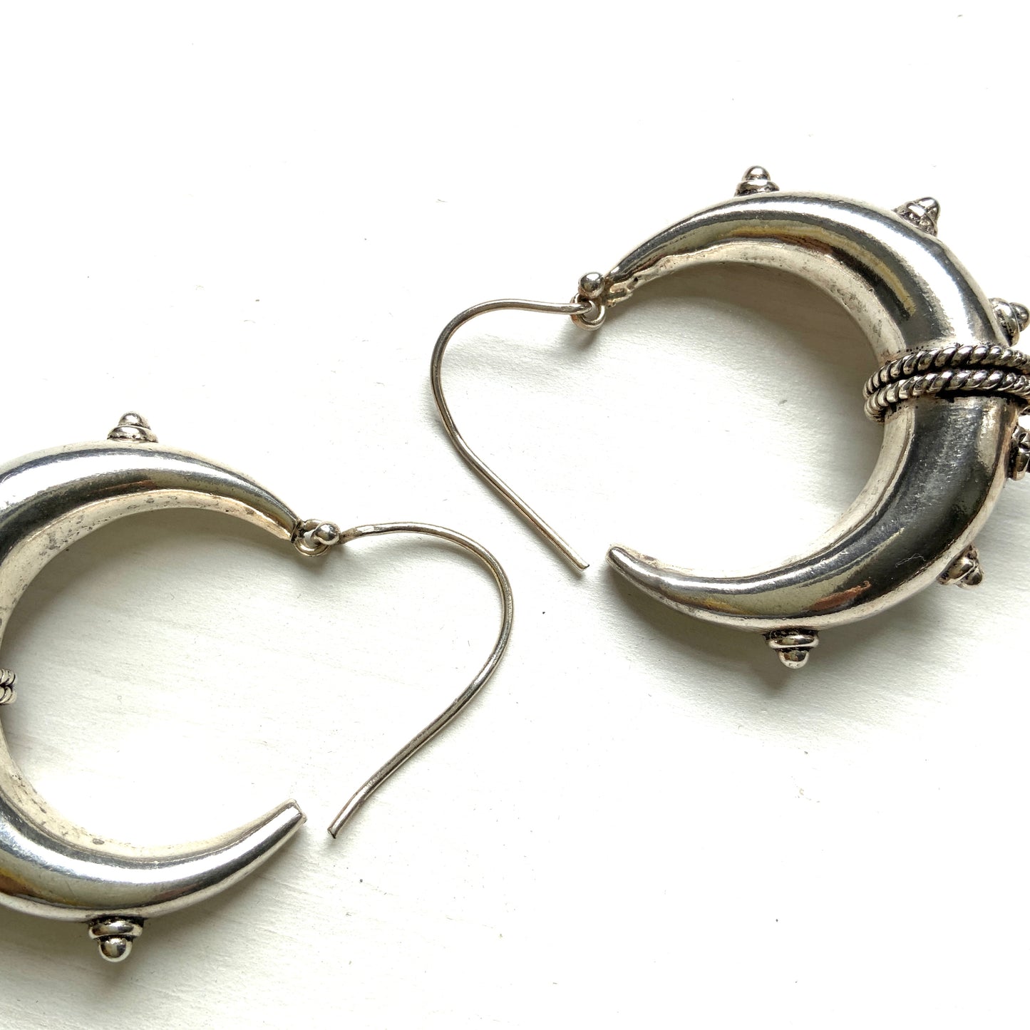 Bold silver hoop earrings in a crescent form, decorated with granulated details and teardrop-shaped protrusions. 三日月型に粒状の装飾とドロップ状の突起をあしらった存在感のあるシルバーフープピアス。
