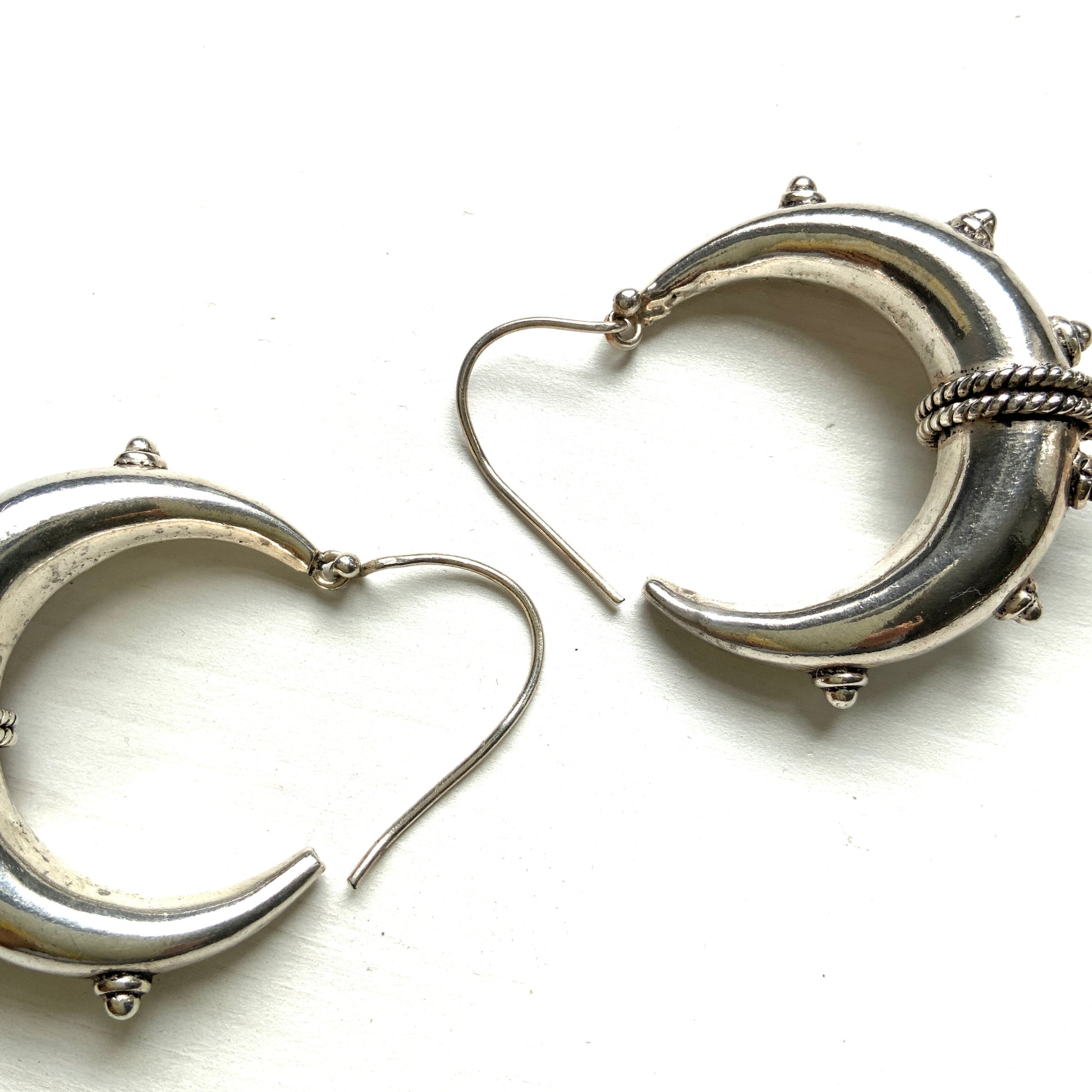 Bold silver hoop earrings in a crescent form, decorated with granulated details and teardrop-shaped protrusions. 三日月型に粒状の装飾とドロップ状の突起をあしらった存在感のあるシルバーフープピアス。