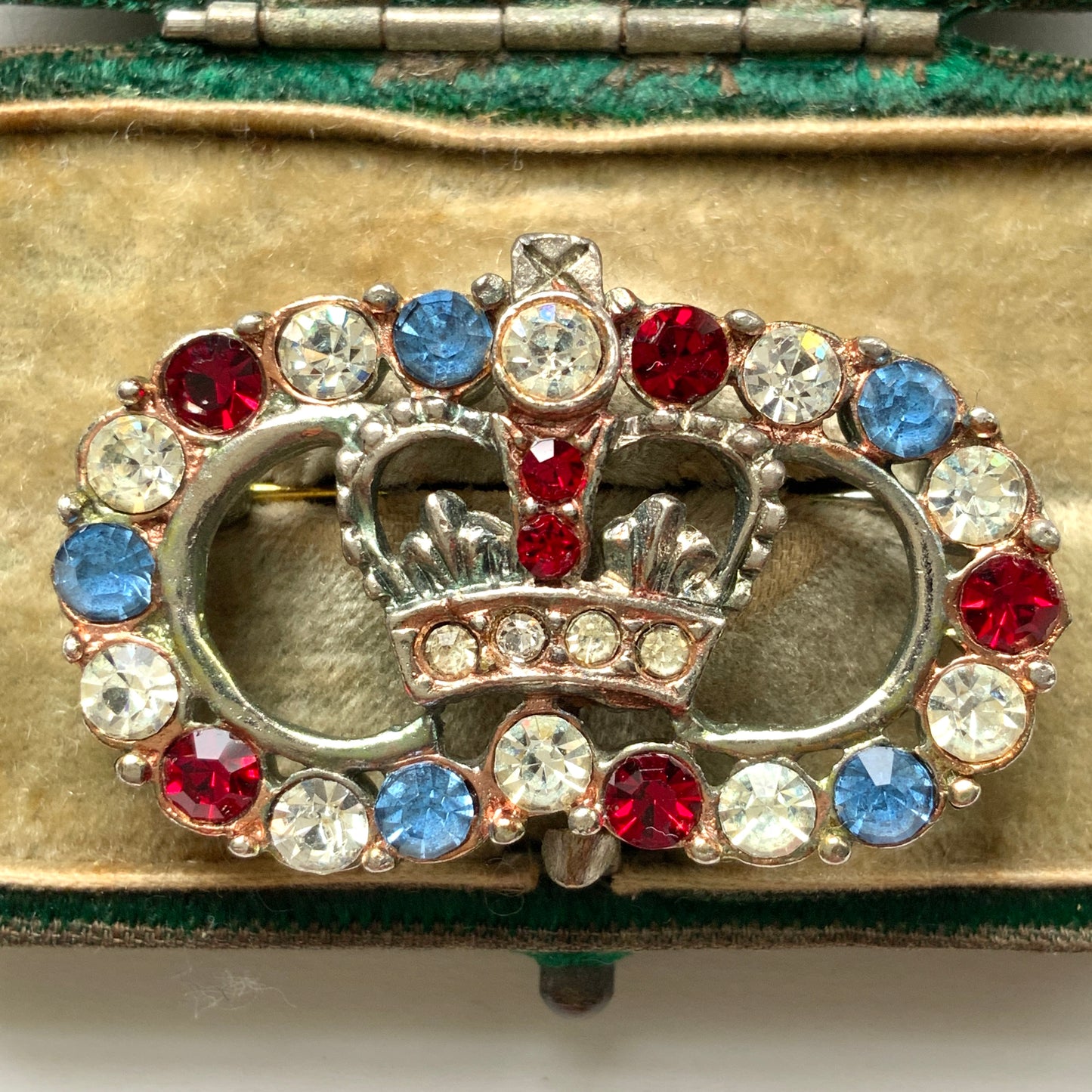 A brooch featuring a crown encircled by tricolour rhinestones – red, clear and blue. 王冠の周りをトリコロールカラーのラインストーンが囲んだブローチ。