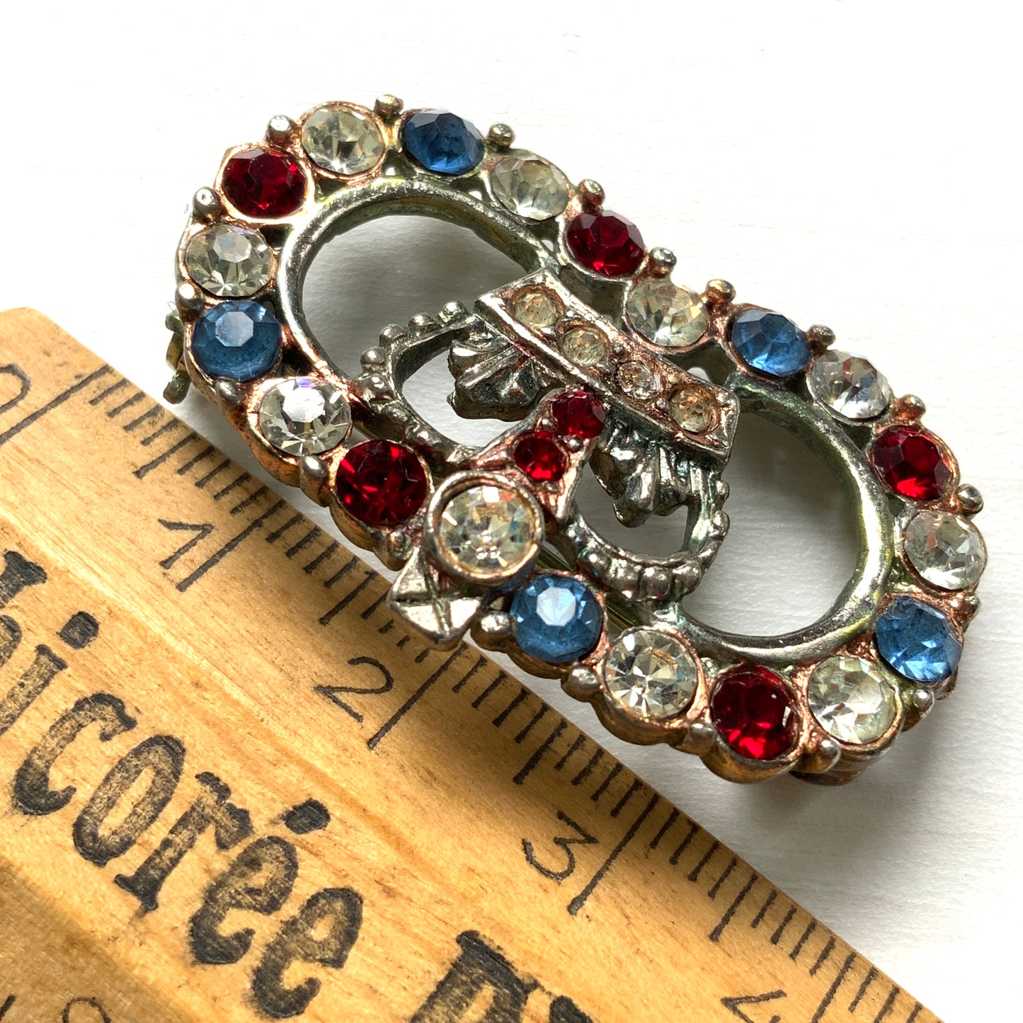 A brooch featuring a crown encircled by tricolour rhinestones – red, clear and blue. 王冠の周りをトリコロールカラーのラインストーンが囲んだブローチ。