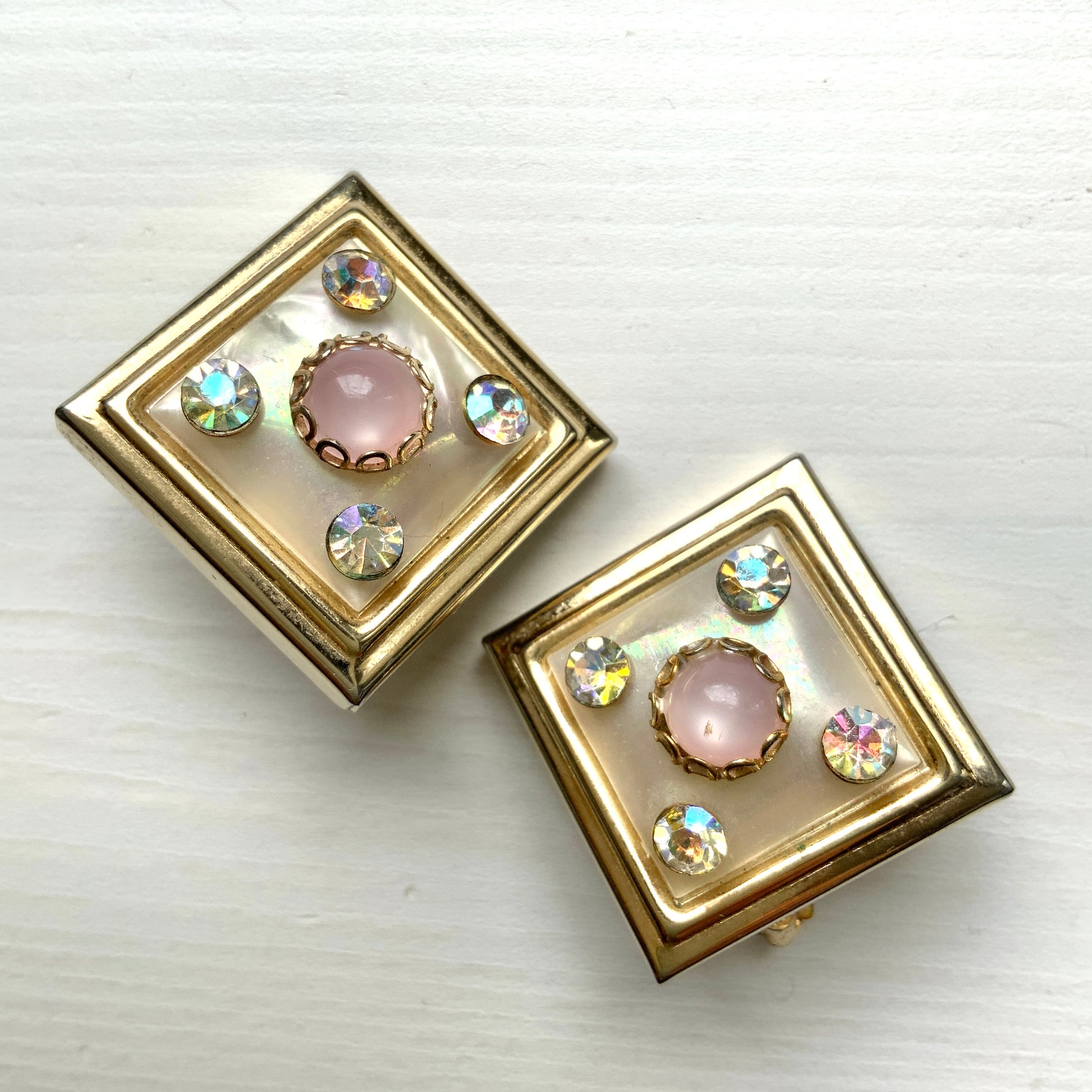 Clip-on earrings featuring white square plastic made to resemble mother of pearl, accented with pink plastic cabochons and shimmering aurora borealis stones. マザーオブパールを模したホワイトのスクエアプラスチックに、ピンクのプラスチックカボションとオーロラストーンが輝くクリップイヤリング。