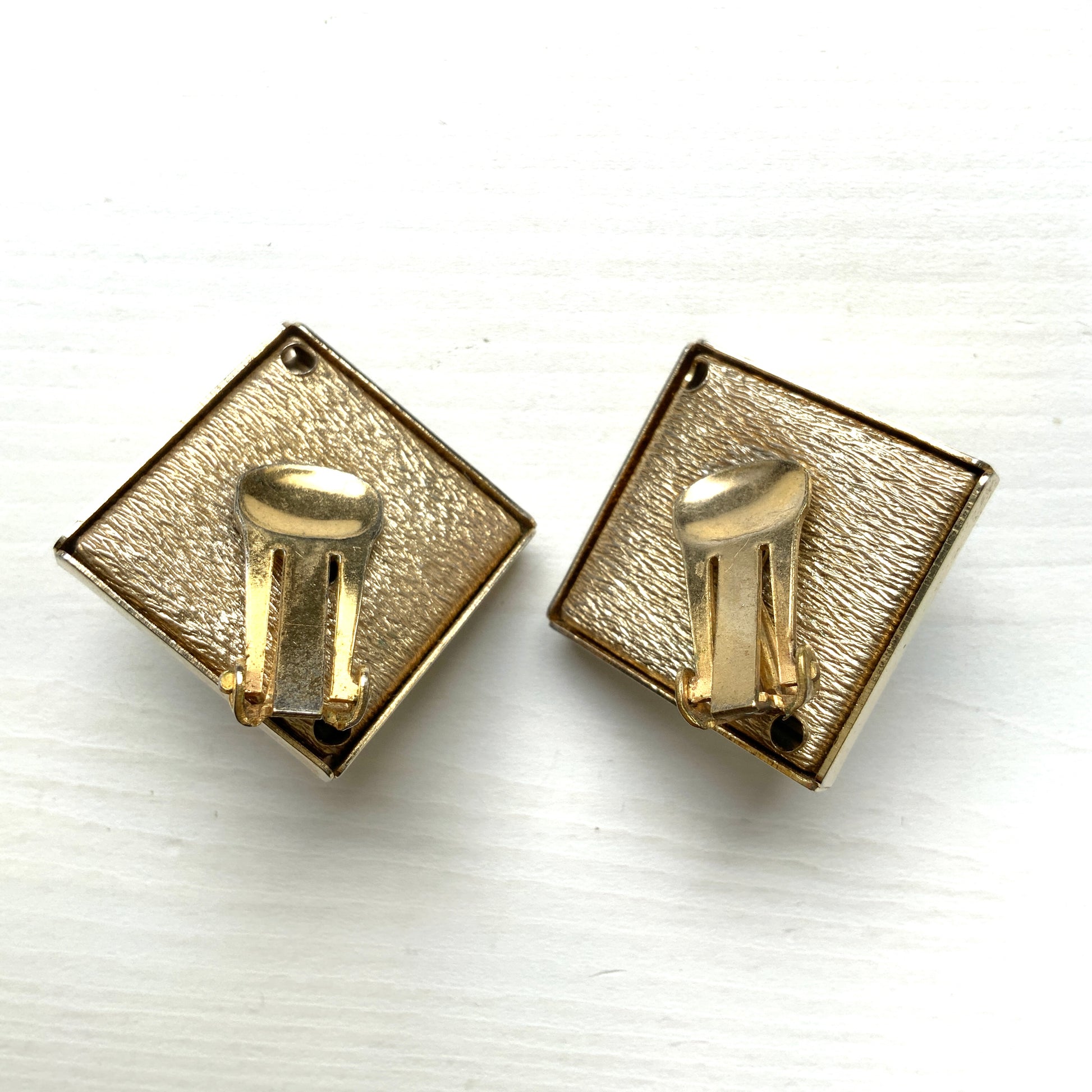 Clip-on earrings featuring white square plastic made to resemble mother of pearl, accented with pink plastic cabochons and shimmering aurora borealis stones. マザーオブパールを模したホワイトのスクエアプラスチックに、ピンクのプラスチックカボションとオーロラストーンが輝くクリップイヤリング。