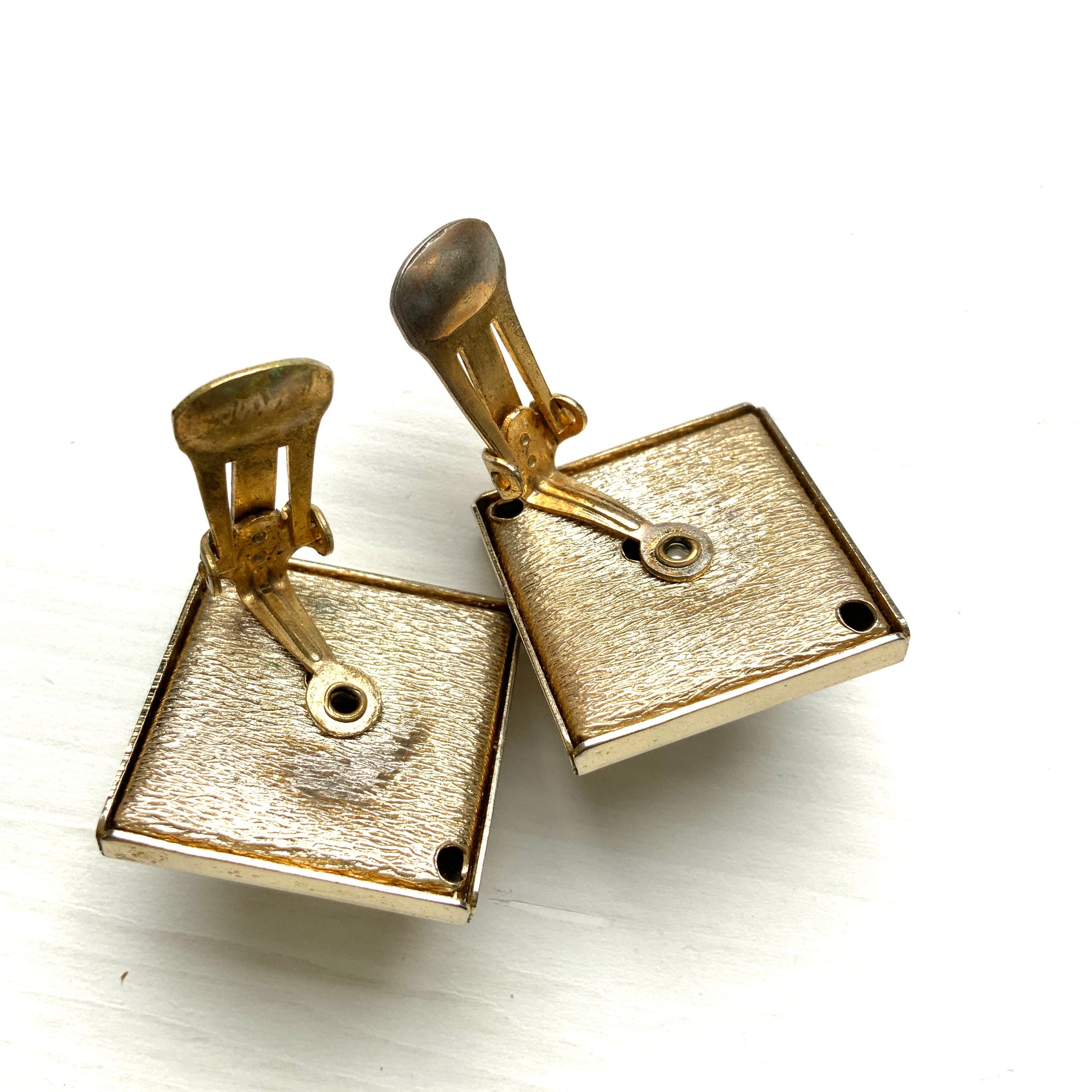 Clip-on earrings featuring white square plastic made to resemble mother of pearl, accented with pink plastic cabochons and shimmering aurora borealis stones. マザーオブパールを模したホワイトのスクエアプラスチックに、ピンクのプラスチックカボションとオーロラストーンが輝くクリップイヤリング。