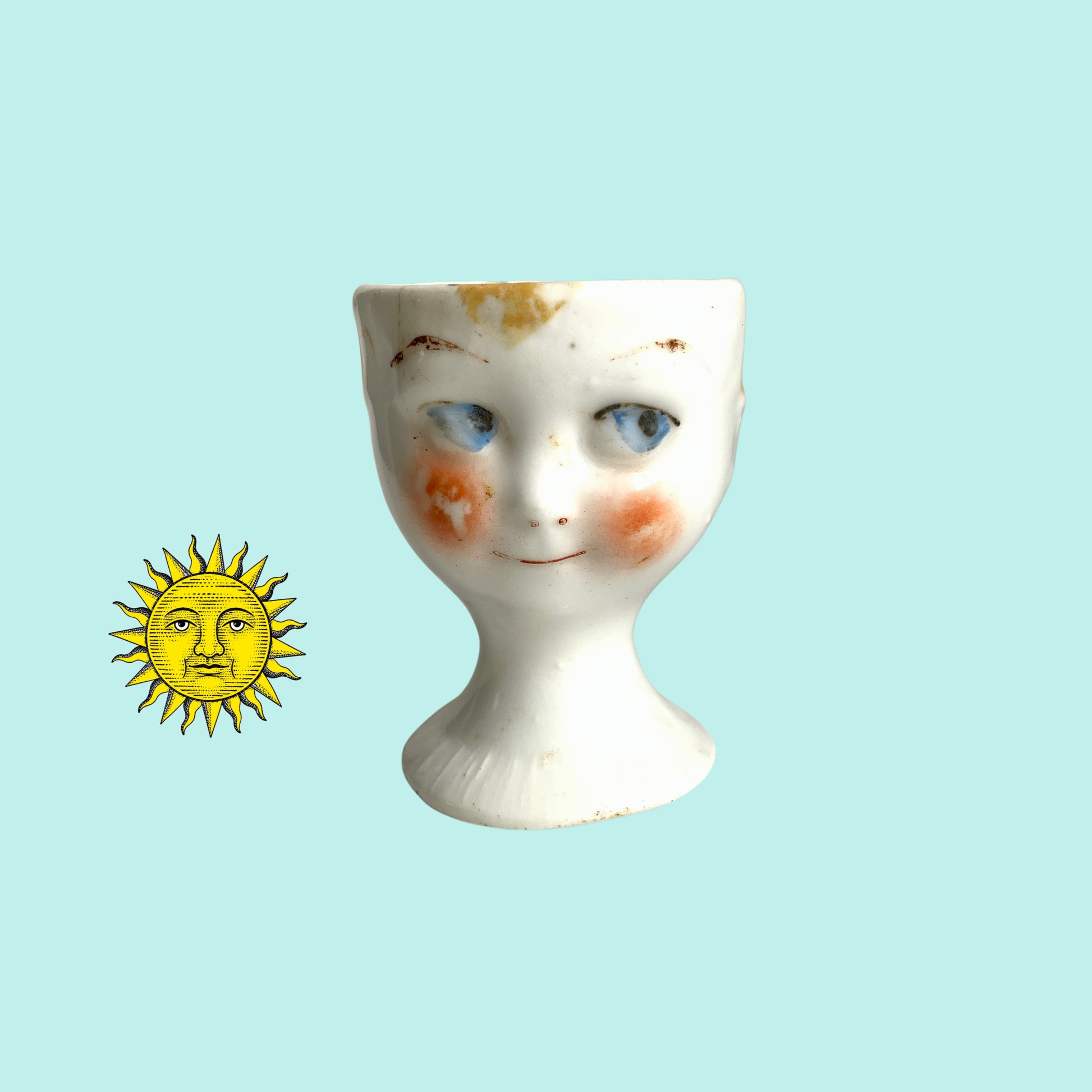 A charming vintage egg cup featuring a smiling child with blue eyes and blonde hair. ブルーアイズとブロンドヘアが印象的な、愛らしい笑顔を浮かべた子どもの顔のヴィンテージエッグカップ。 