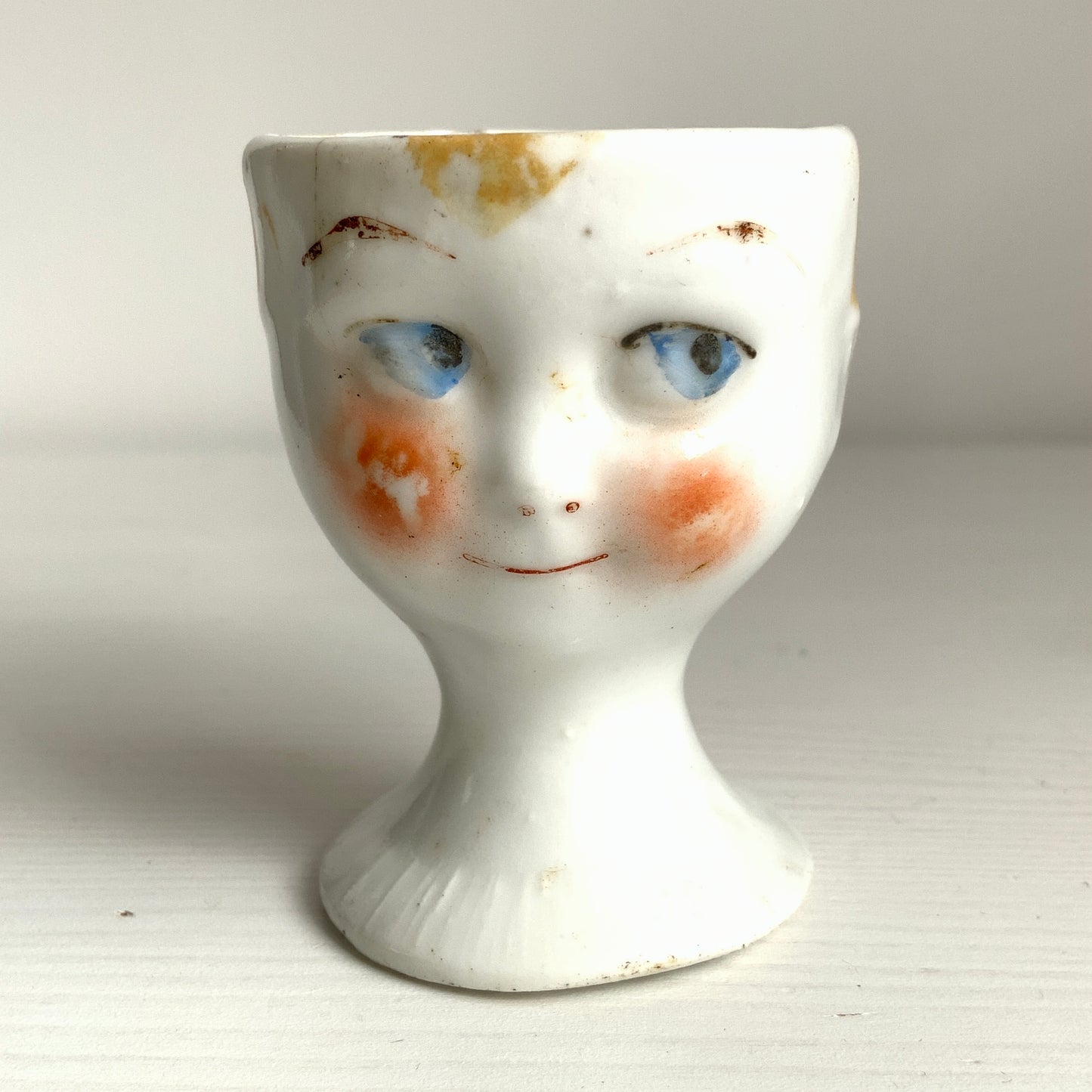 A charming vintage egg cup featuring a smiling child with blue eyes and blonde hair. ブルーアイズとブロンドヘアが印象的な、愛らしい笑顔を浮かべた子どもの顔のヴィンテージエッグカップ。 