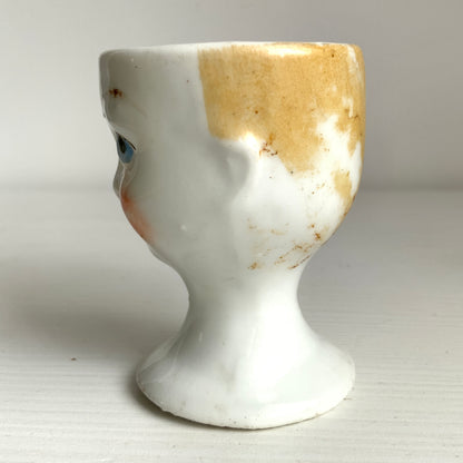 A charming vintage egg cup featuring a smiling child with blue eyes and blonde hair. ブルーアイズとブロンドヘアが印象的な、愛らしい笑顔を浮かべた子どもの顔のヴィンテージエッグカップ。 