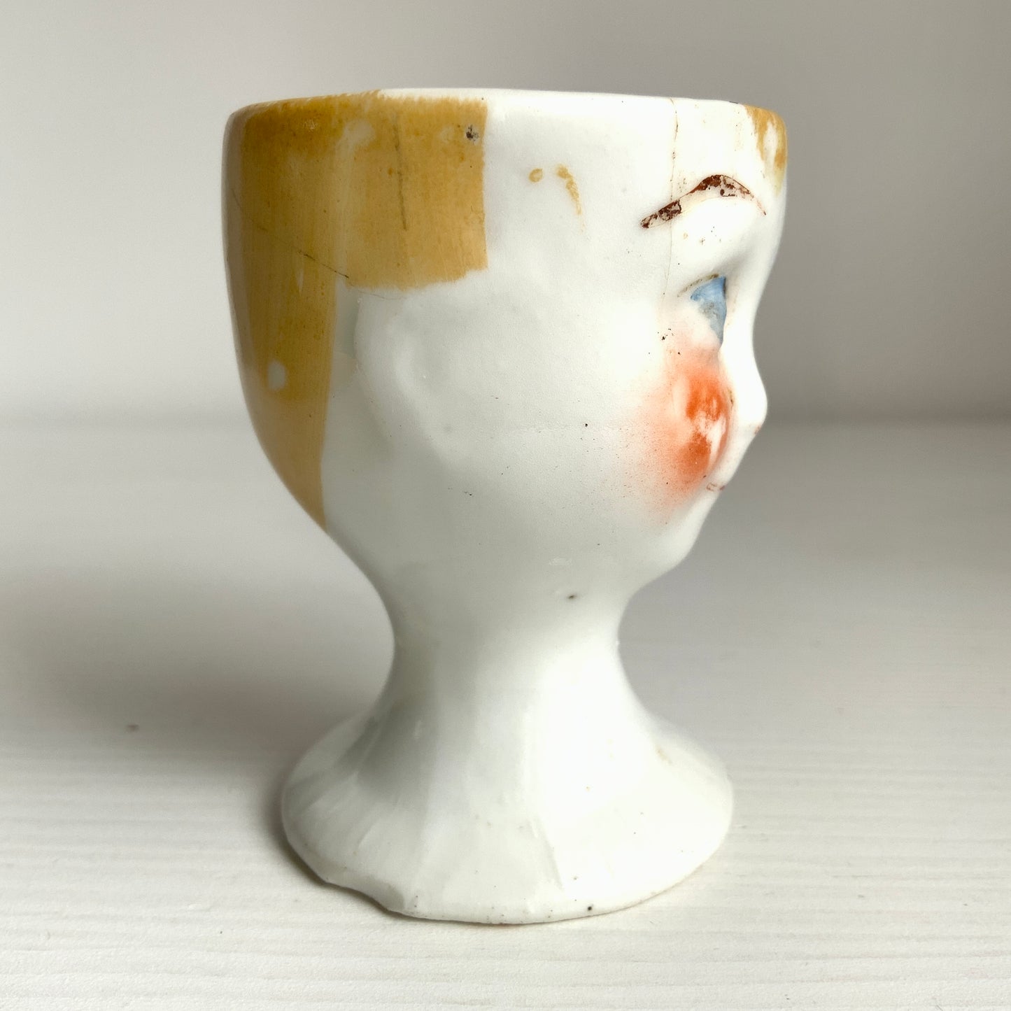 A charming vintage egg cup featuring a smiling child with blue eyes and blonde hair. ブルーアイズとブロンドヘアが印象的な、愛らしい笑顔を浮かべた子どもの顔のヴィンテージエッグカップ。 