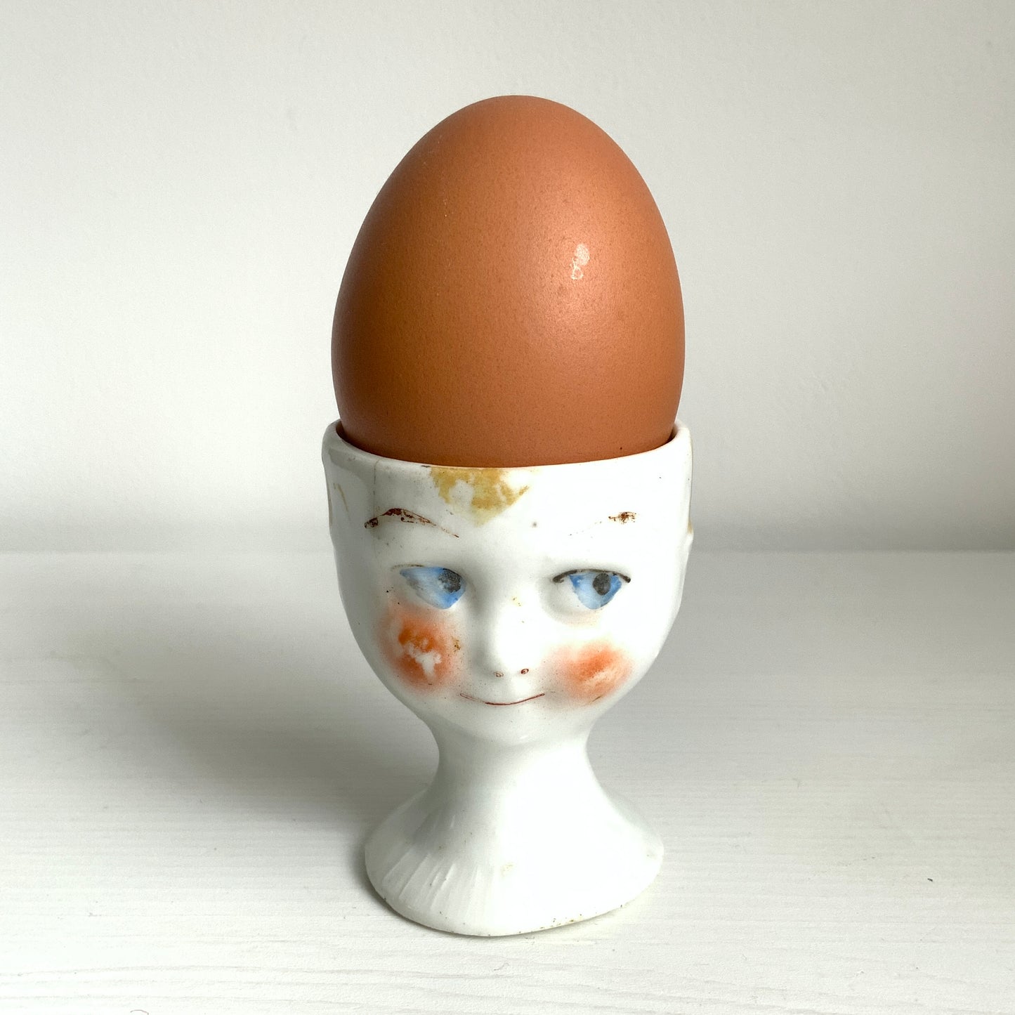 A charming vintage egg cup featuring a smiling child with blue eyes and blonde hair. ブルーアイズとブロンドヘアが印象的な、愛らしい笑顔を浮かべた子どもの顔のヴィンテージエッグカップ。 