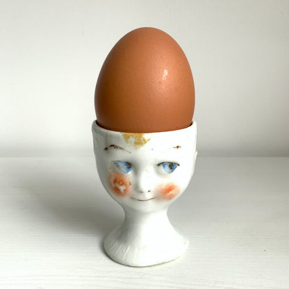 A charming vintage egg cup featuring a smiling child with blue eyes and blonde hair. ブルーアイズとブロンドヘアが印象的な、愛らしい笑顔を浮かべた子どもの顔のヴィンテージエッグカップ。 