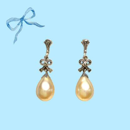 A pair of screw-back earrings featuring teardrop glass pearls suspended from silver bows. シルバー製のリボンに、ティアドロップのグラスパールが揺れるスクリューイヤリング。