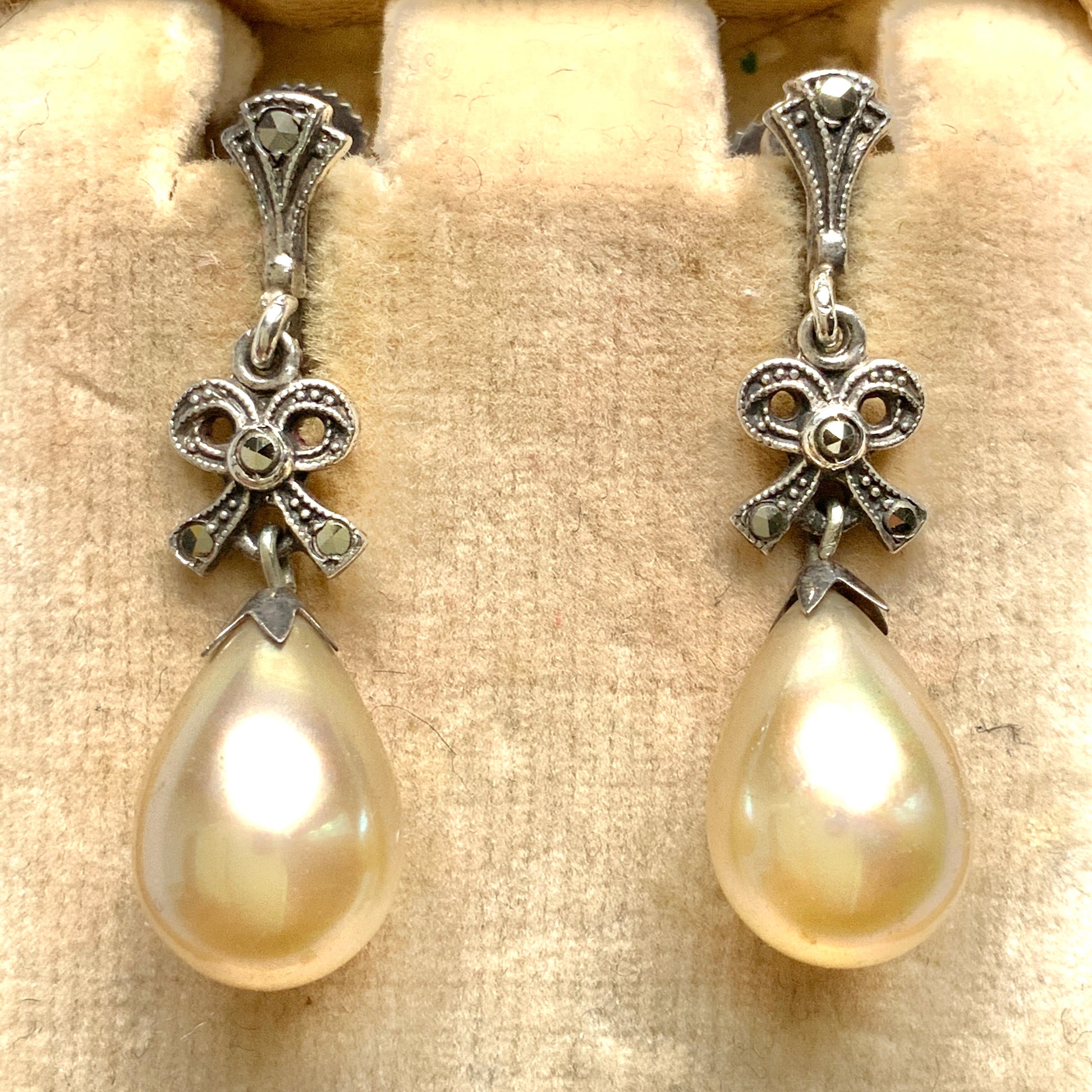 A pair of screw-back earrings featuring teardrop glass pearls suspended from silver bows. シルバー製のリボンに、ティアドロップのグラスパールが揺れるスクリューイヤリング。