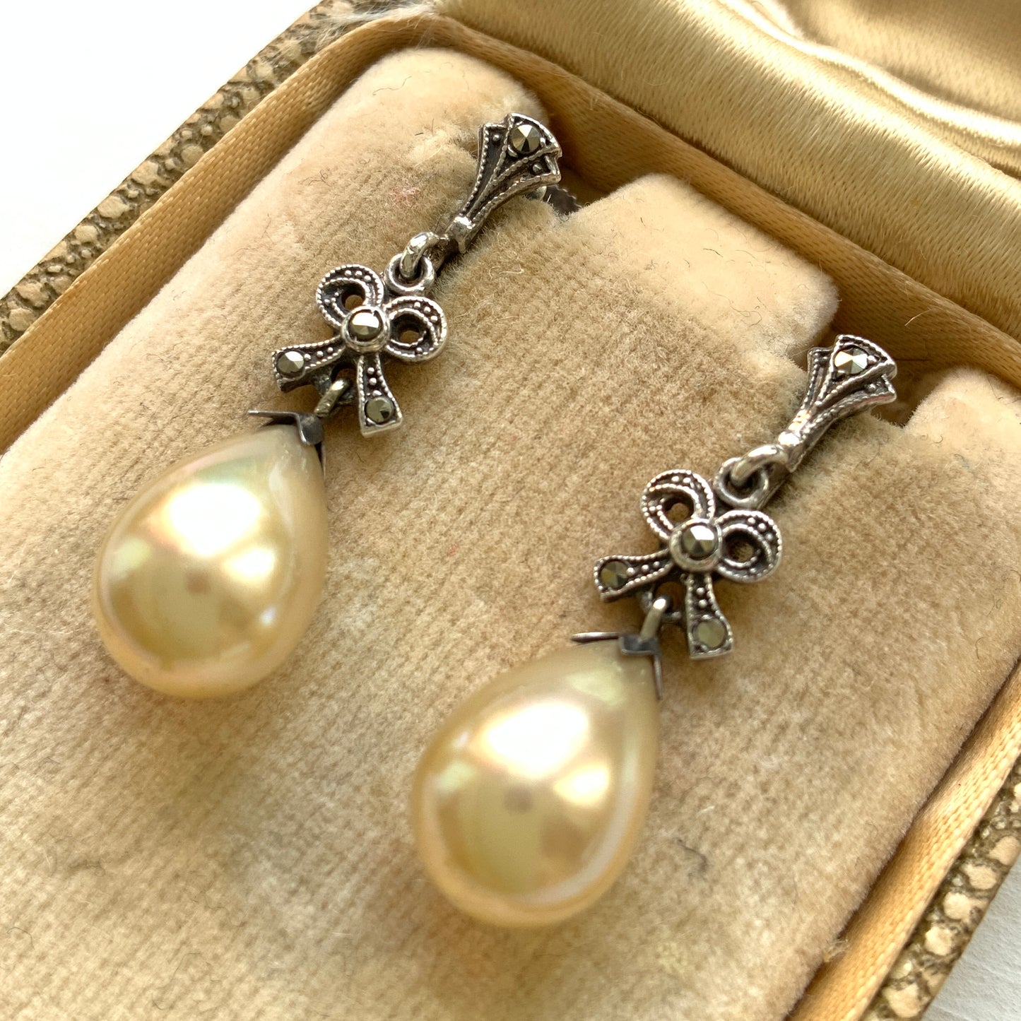A pair of screw-back earrings featuring teardrop glass pearls suspended from silver bows. シルバー製のリボンに、ティアドロップのグラスパールが揺れるスクリューイヤリング。