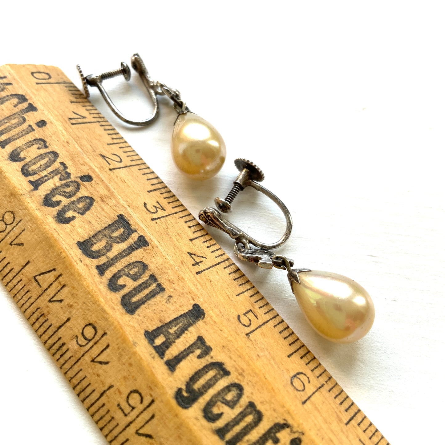 A pair of screw-back earrings featuring teardrop glass pearls suspended from silver bows. シルバー製のリボンに、ティアドロップのグラスパールが揺れるスクリューイヤリング。