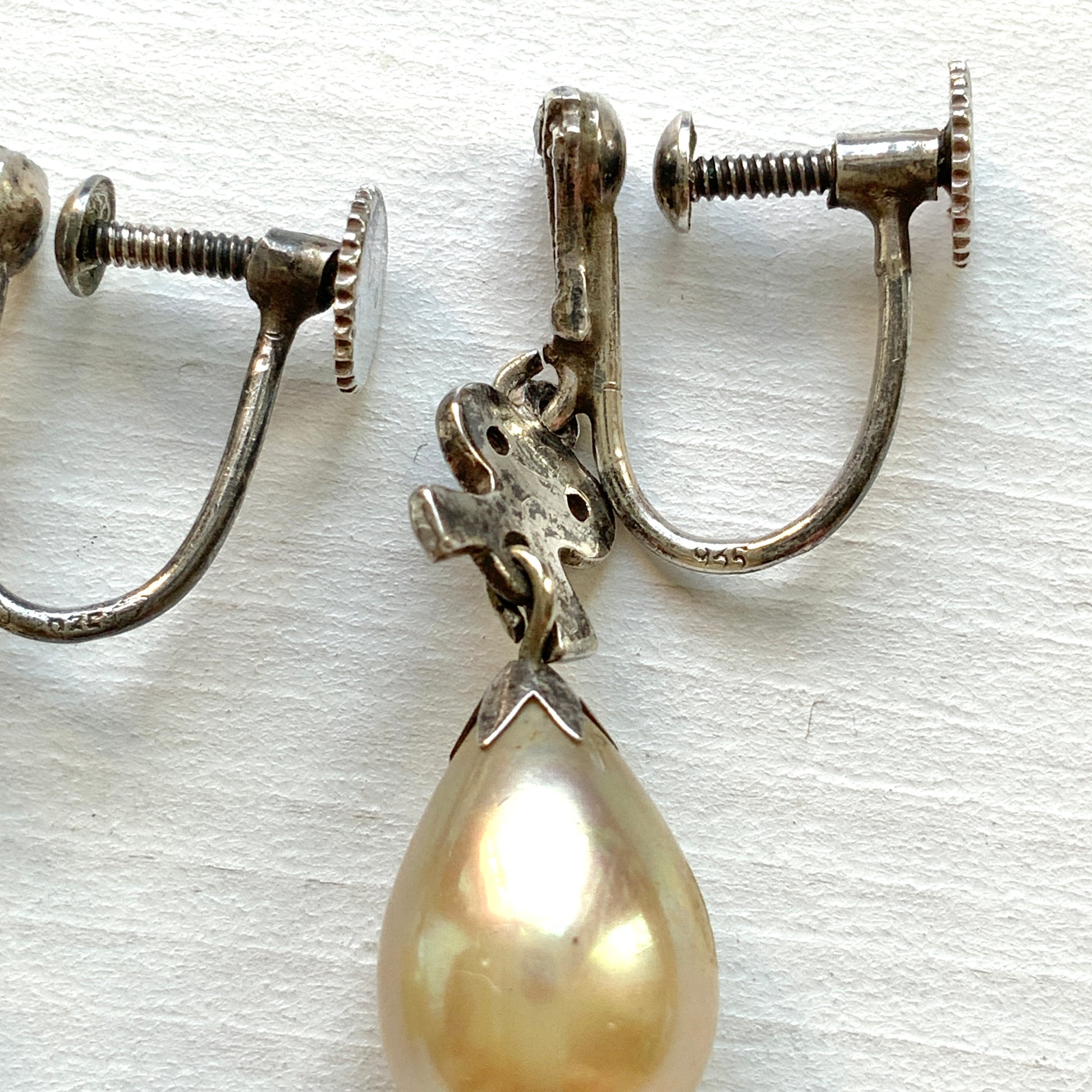 A pair of screw-back earrings featuring teardrop glass pearls suspended from silver bows. シルバー製のリボンに、ティアドロップのグラスパールが揺れるスクリューイヤリング。