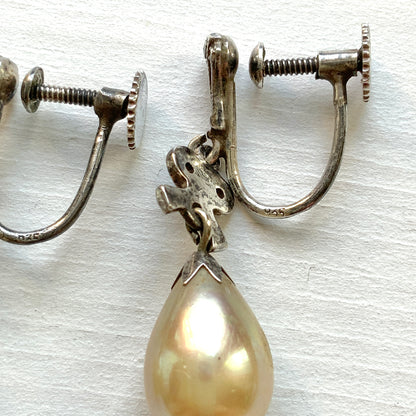 A pair of screw-back earrings featuring teardrop glass pearls suspended from silver bows. シルバー製のリボンに、ティアドロップのグラスパールが揺れるスクリューイヤリング。