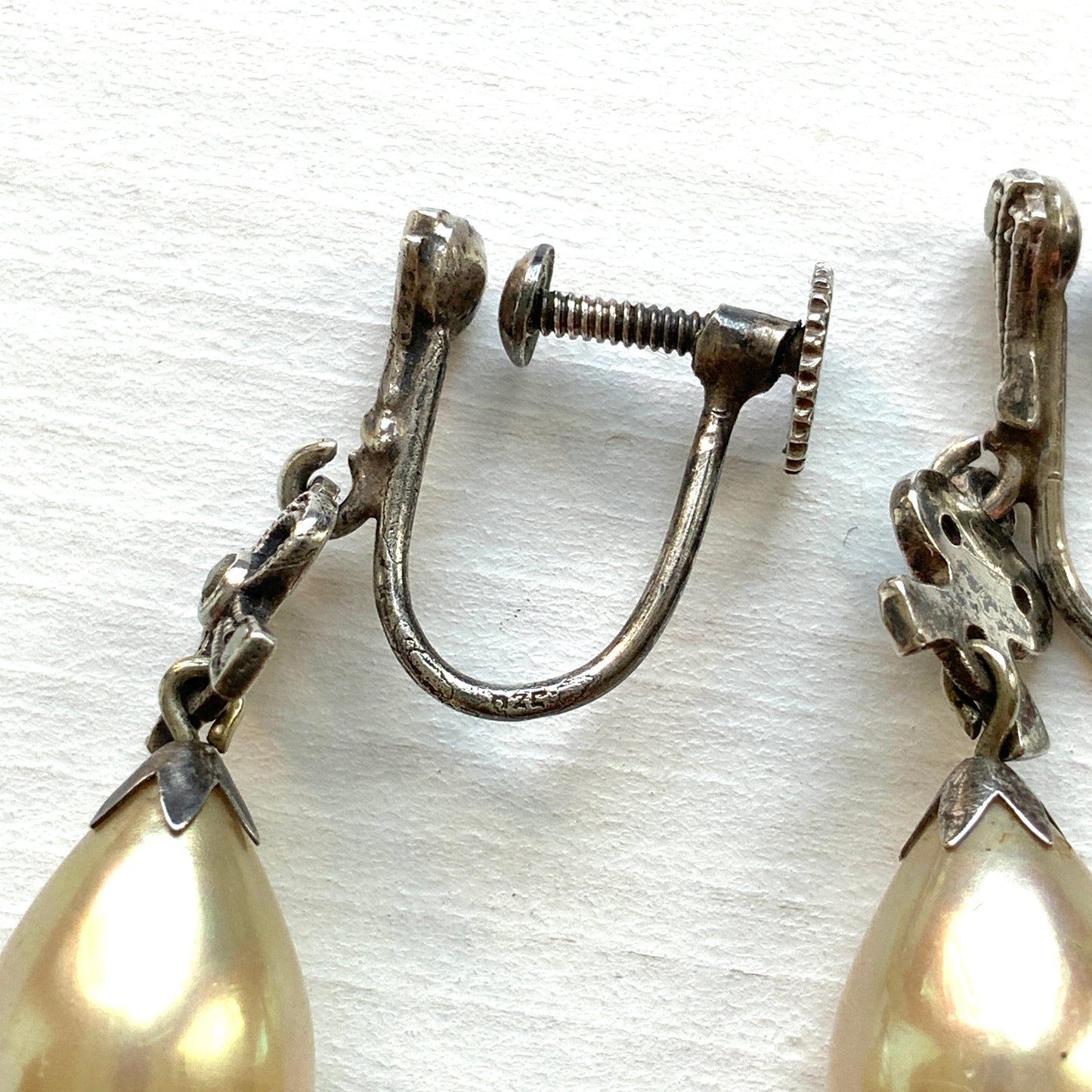 A pair of screw-back earrings featuring teardrop glass pearls suspended from silver bows. シルバー製のリボンに、ティアドロップのグラスパールが揺れるスクリューイヤリング。