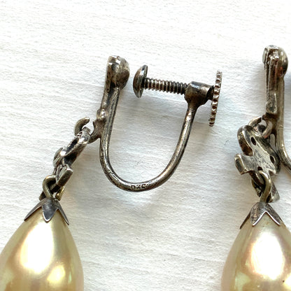 A pair of screw-back earrings featuring teardrop glass pearls suspended from silver bows. シルバー製のリボンに、ティアドロップのグラスパールが揺れるスクリューイヤリング。