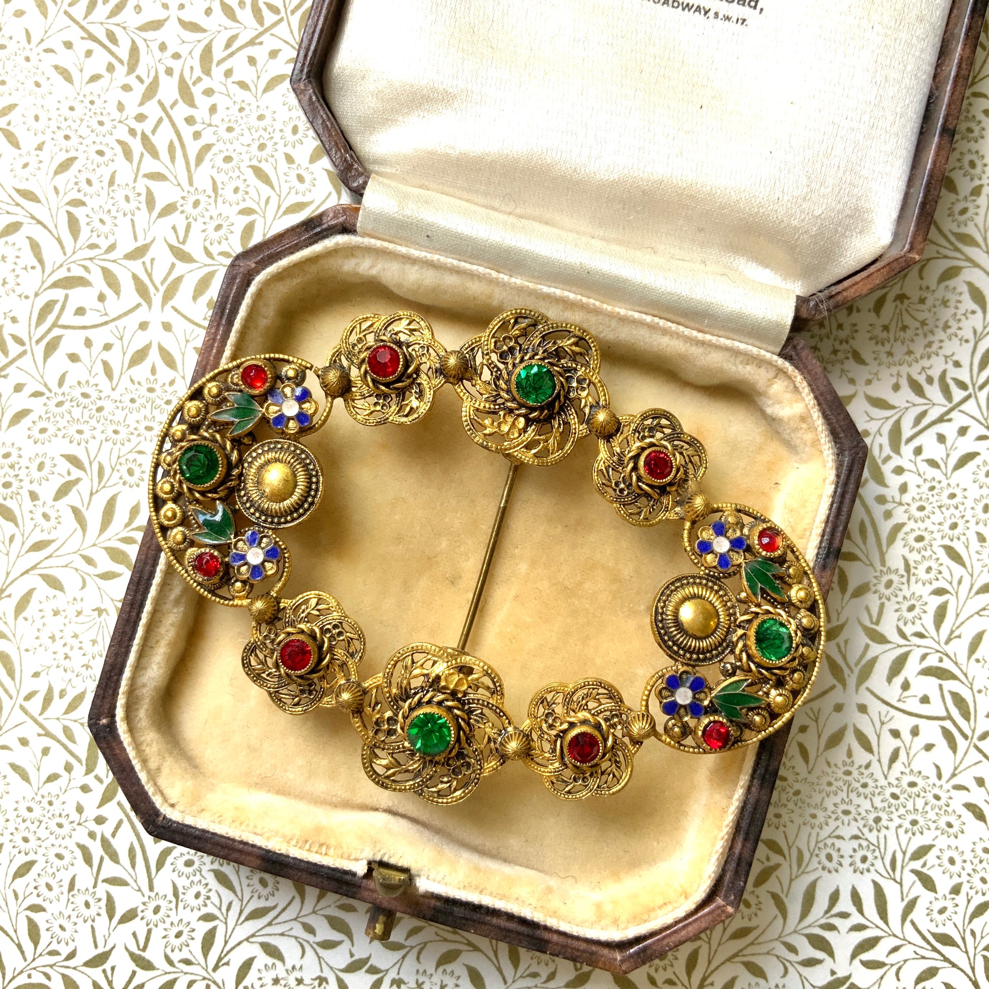 A buckle-style brooch composed of various filigree plates, adorned with colourful rhinestones and enamel details.  様々な形のフィリグリー プレートを繋げ、そこにカラフルなラインストーン やエナメル をあしらったバックル型のブローチ。