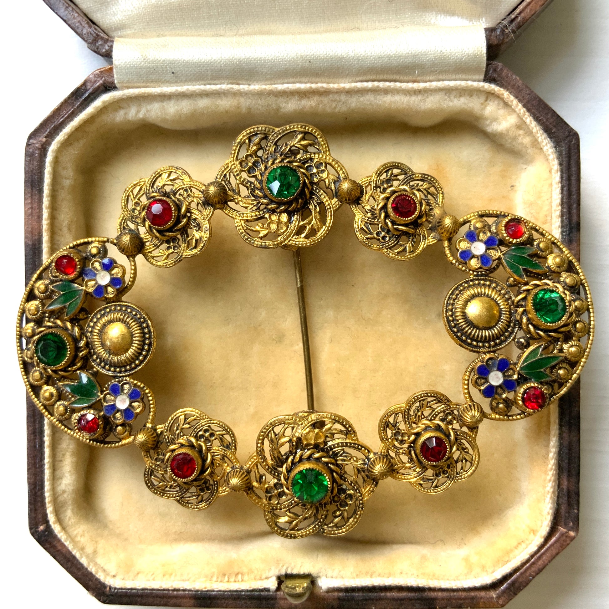 A buckle-style brooch composed of various filigree plates, adorned with colourful rhinestones and enamel details.  様々な形のフィリグリー プレートを繋げ、そこにカラフルなラインストーン やエナメル をあしらったバックル型のブローチ。