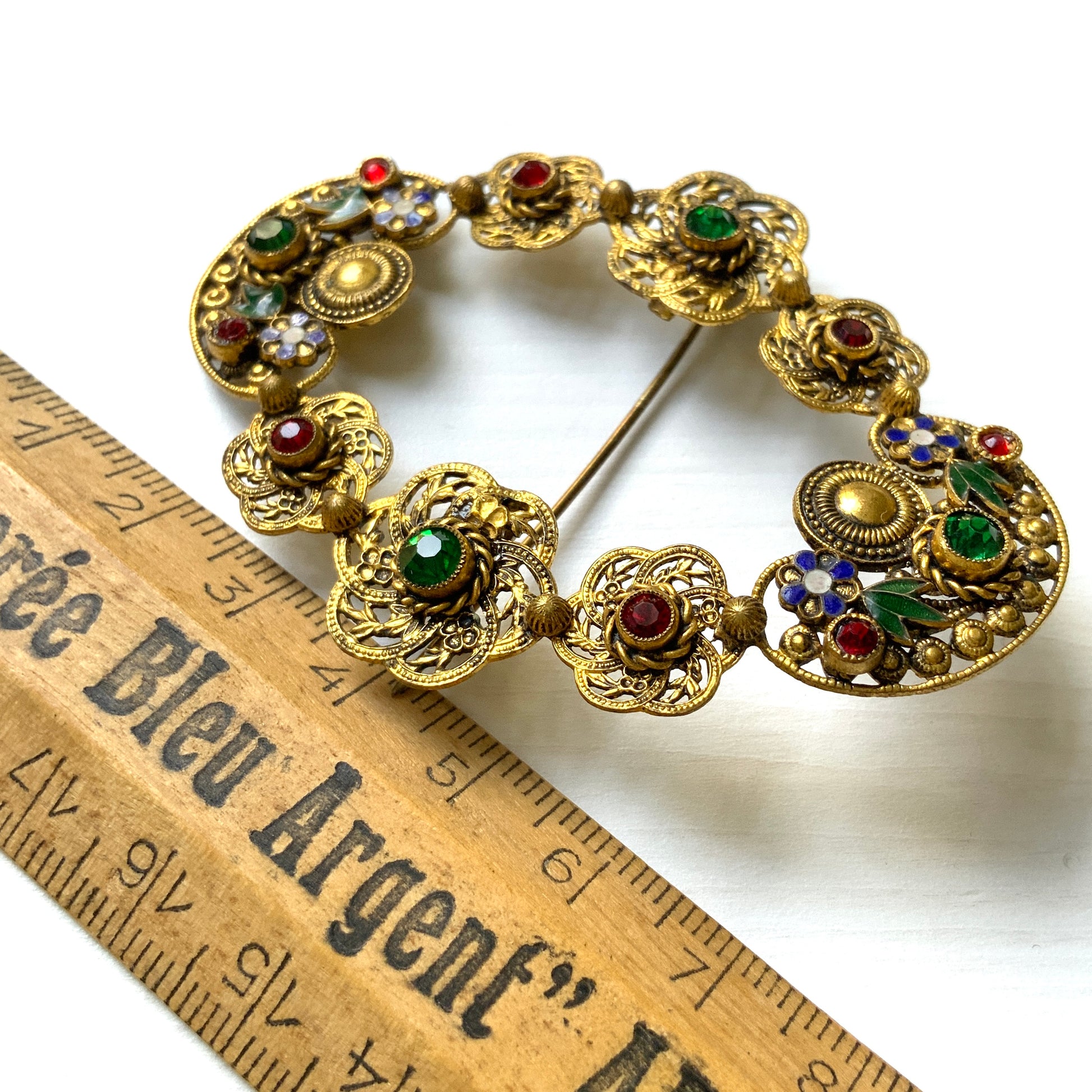 A buckle-style brooch composed of various filigree plates, adorned with colourful rhinestones and enamel details.  様々な形のフィリグリー プレートを繋げ、そこにカラフルなラインストーン やエナメル をあしらったバックル型のブローチ。