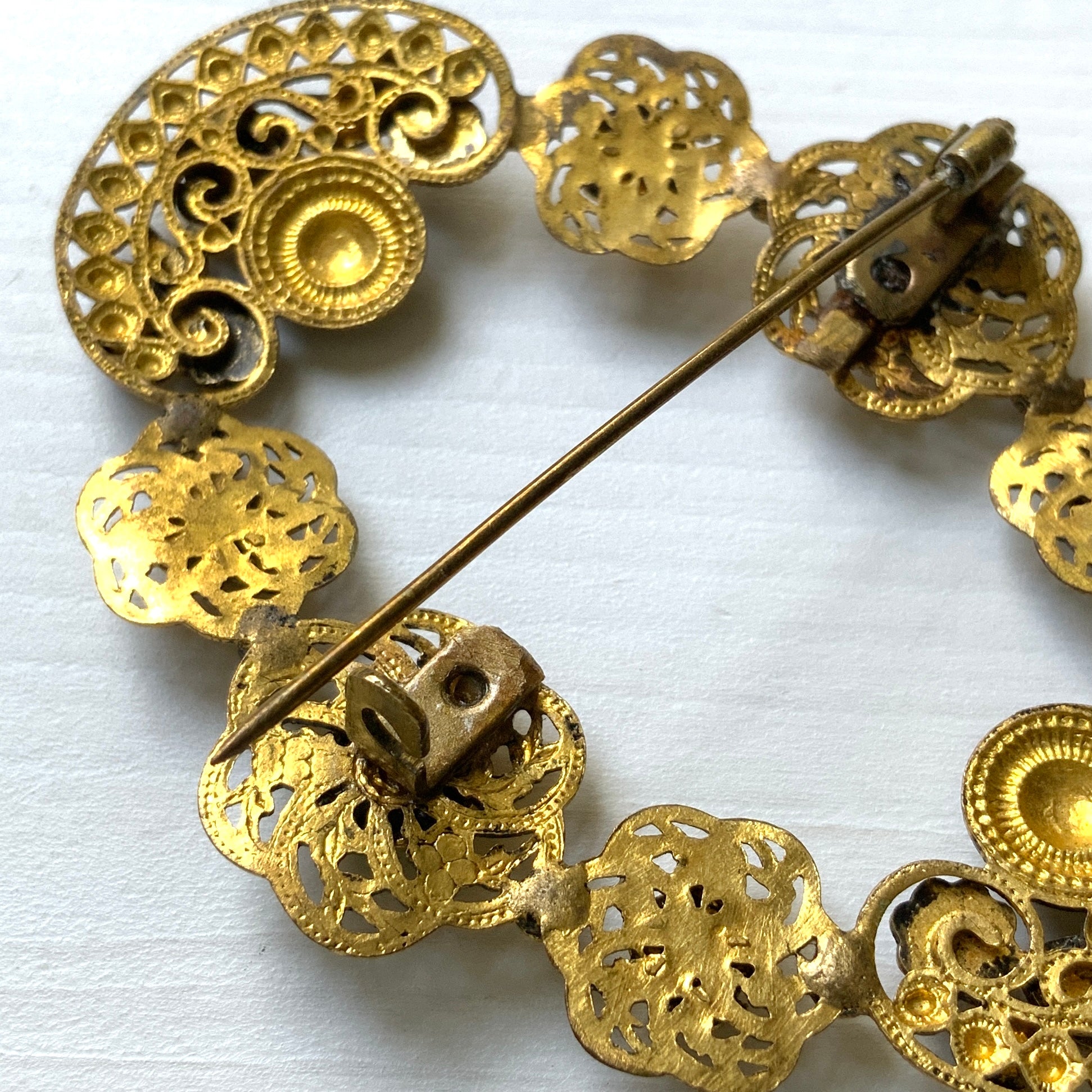 A buckle-style brooch composed of various filigree plates, adorned with colourful rhinestones and enamel details.  様々な形のフィリグリー プレートを繋げ、そこにカラフルなラインストーン やエナメル をあしらったバックル型のブローチ。