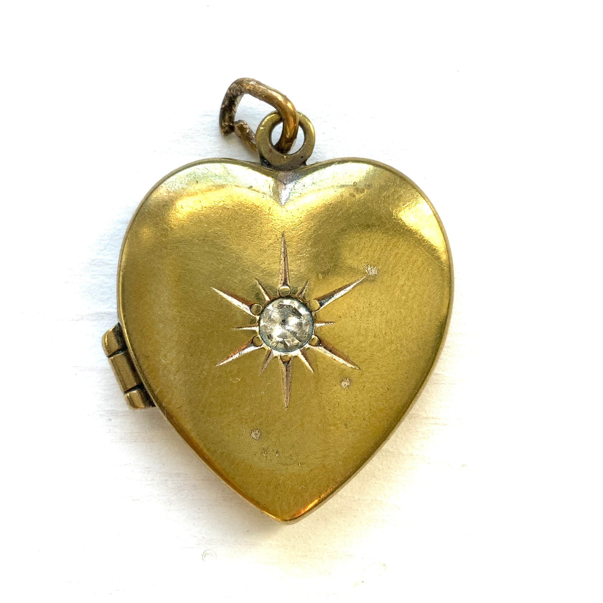 A gold-filled heart-shaped locket adorned with a small starburst motif. 小さなスターバーストモチーフがあしらわれた、ゴールドフィルドのハート型のロケット。
