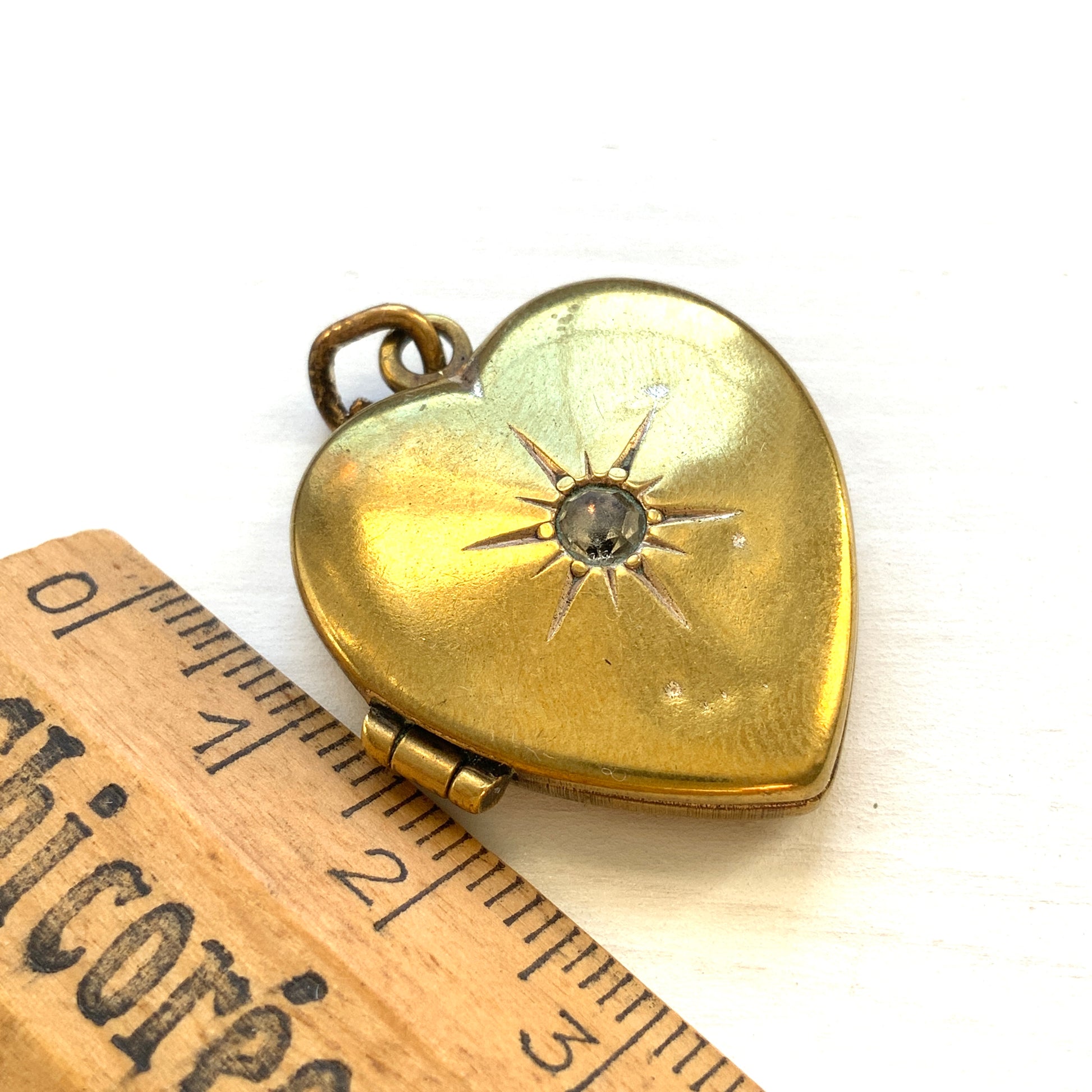 A gold-filled heart-shaped locket adorned with a small starburst motif. 小さなスターバーストモチーフがあしらわれた、ゴールドフィルドのハート型のロケット。