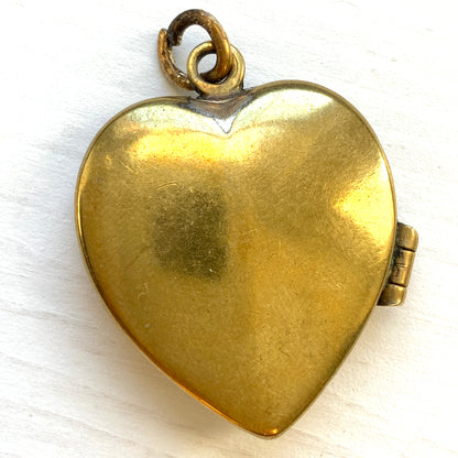 A gold-filled heart-shaped locket adorned with a small starburst motif. 小さなスターバーストモチーフがあしらわれた、ゴールドフィルドのハート型のロケット。