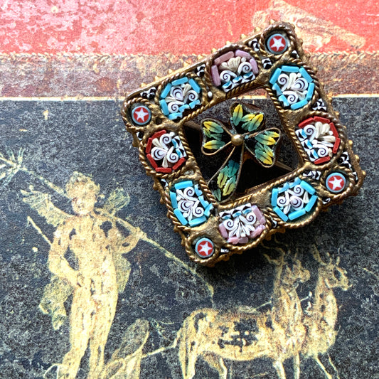 A brooch featuring a three-leaf clover set inside a diamond-shaped frame adorned with delicate detailing. 細かな飾りが飾られたダイヤ型のフレームの中に、三つ葉のクローバーが入ったブローチ。 