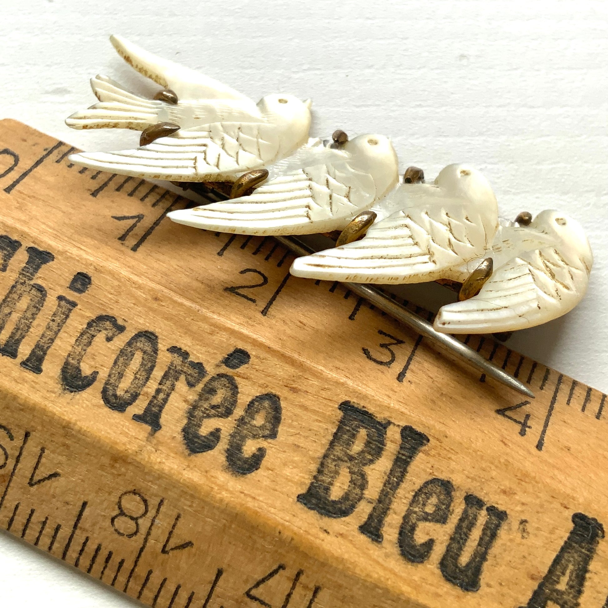 A brooch carved from mother of pearl, depicting a group of small birds. マザーオブパールに彫り出された小さな鳥たちのブローチ。