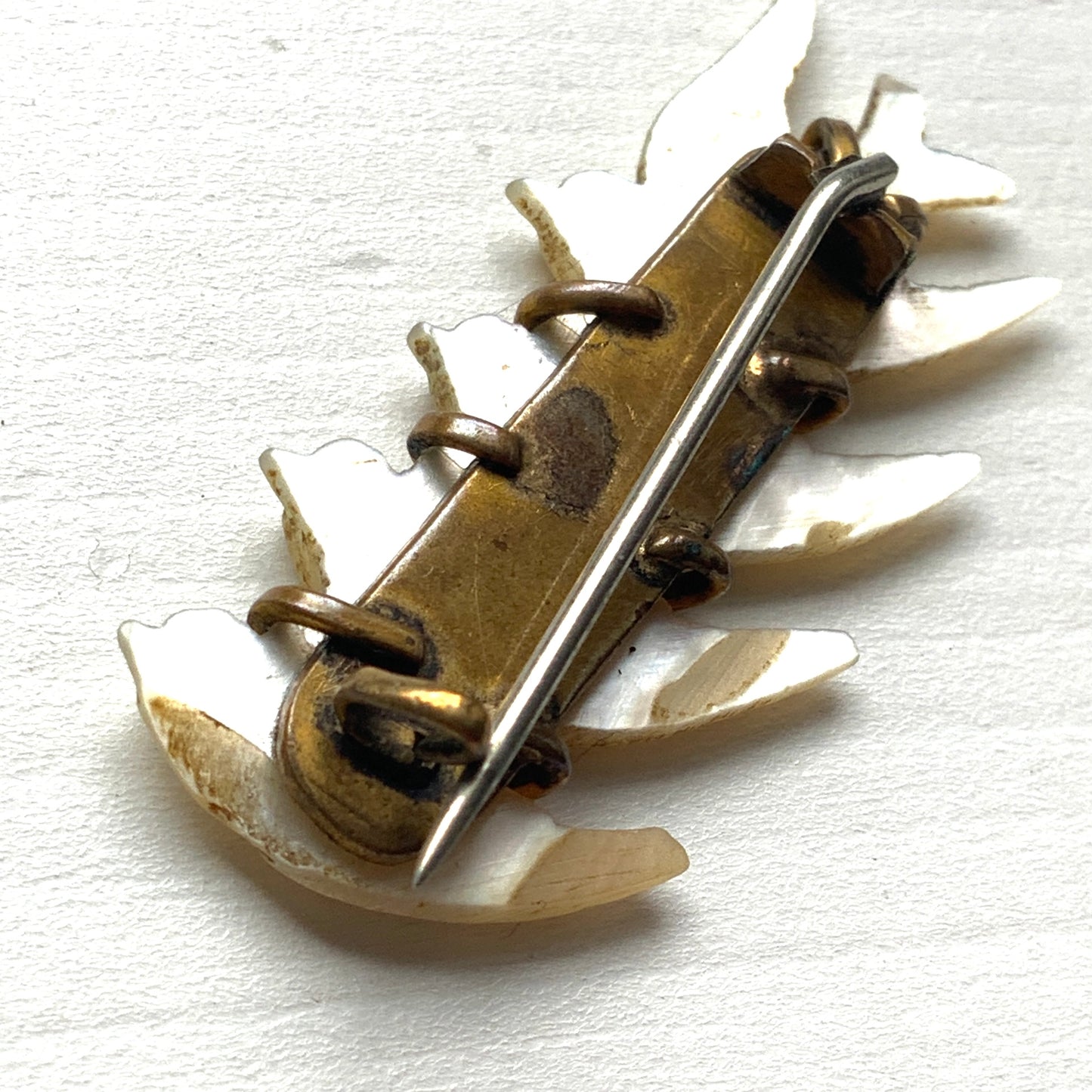 A brooch carved from mother of pearl, depicting a group of small birds. マザーオブパールに彫り出された小さな鳥たちのブローチ。