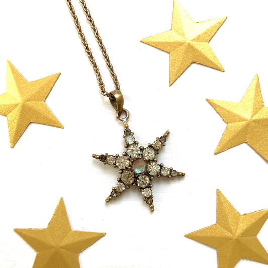 An antique pendant necklace featuring a starburst design with a mysterious glass stone known as Saphiret set in the centre. 神秘的な輝きを放つサフィレットを中央に添えた、ラインストーンのスターバーストデザインのペンダントネックレス。