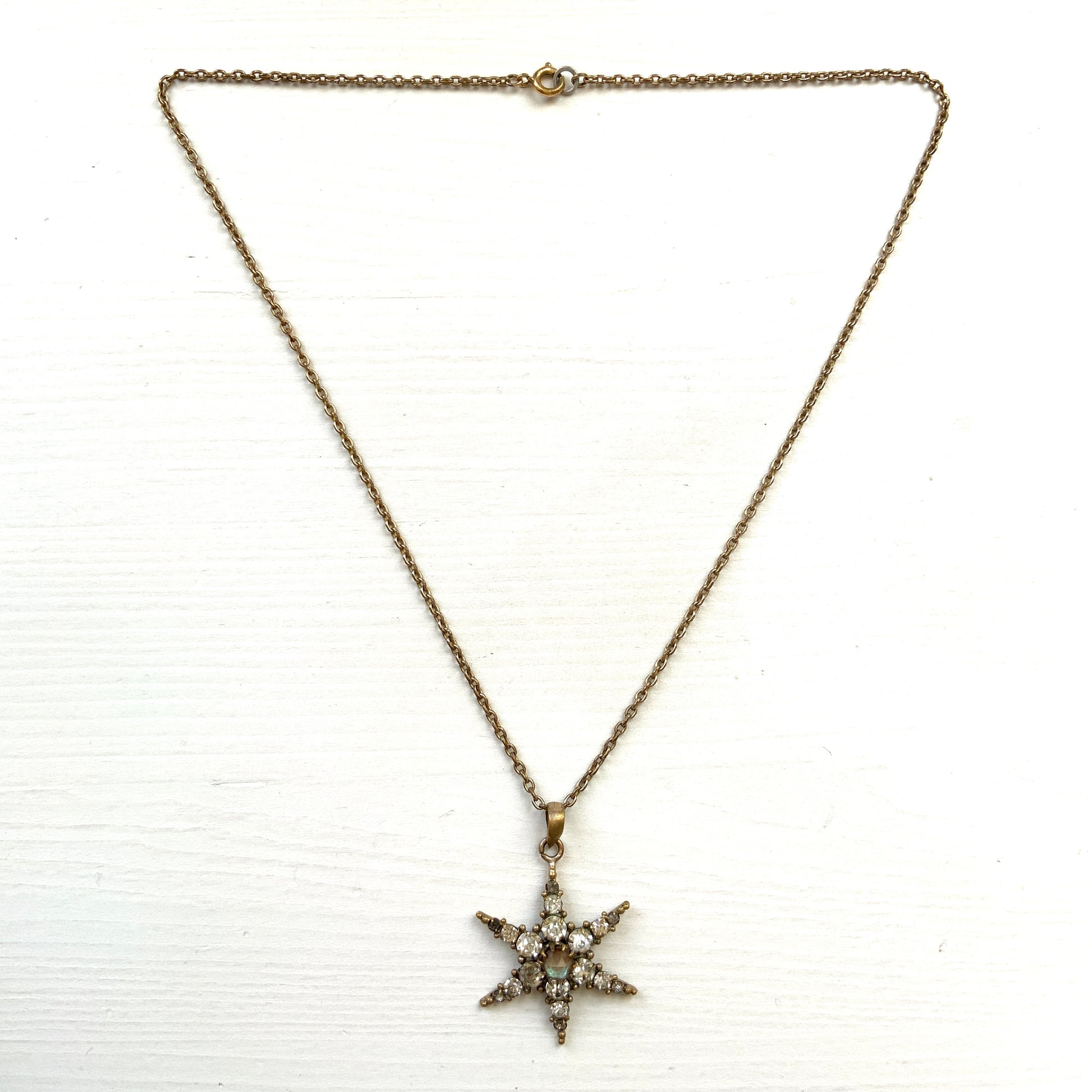 An antique pendant necklace featuring a starburst design with a mysterious glass stone known as Saphiret set in the centre. 神秘的な輝きを放つサフィレットを中央に添えた、ラインストーンのスターバーストデザインのペンダントネックレス。