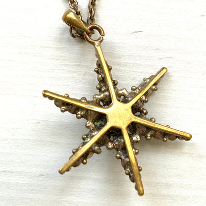 An antique pendant necklace featuring a starburst design with a mysterious glass stone known as Saphiret set in the centre. 神秘的な輝きを放つサフィレットを中央に添えた、ラインストーンのスターバーストデザインのペンダントネックレス。