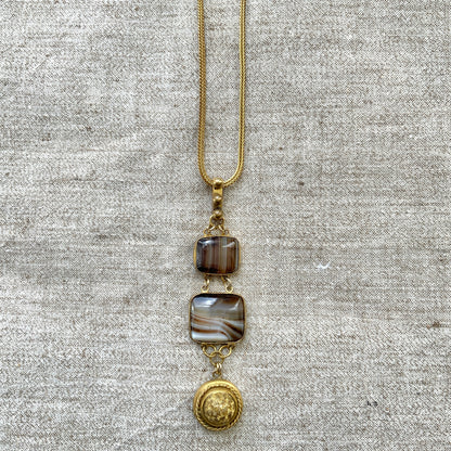 A lavaliere necklace featuring beautifully banded brown and white agate, paired with a gold-tone charm. ブラウンとホワイトの縞模様が美しいメノウと、ゴールドトーンのチャームが組み合わされたラヴァリエネックレス。