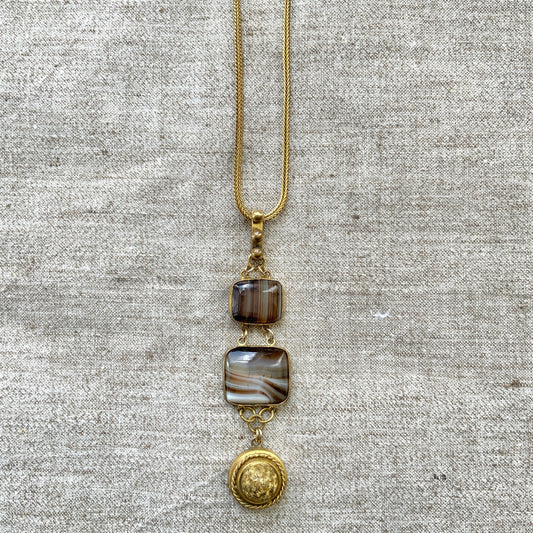 A lavaliere necklace featuring beautifully banded brown and white agate, paired with a gold-tone charm. ブラウンとホワイトの縞模様が美しいメノウと、ゴールドトーンのチャームが組み合わされたラヴァリエネックレス。