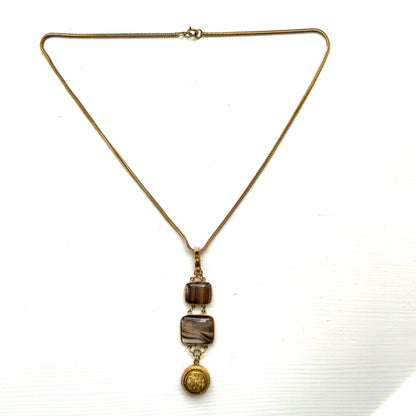 A lavaliere necklace featuring beautifully banded brown and white agate, paired with a gold-tone charm. ブラウンとホワイトの縞模様が美しいメノウと、ゴールドトーンのチャームが組み合わされたラヴァリエネックレス。