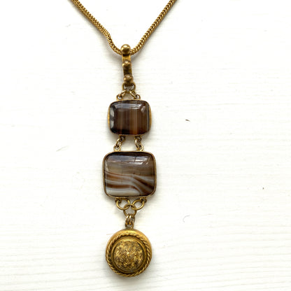 A lavaliere necklace featuring beautifully banded brown and white agate, paired with a gold-tone charm. ブラウンとホワイトの縞模様が美しいメノウと、ゴールドトーンのチャームが組み合わされたラヴァリエネックレス。
