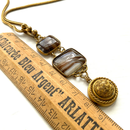 A lavaliere necklace featuring beautifully banded brown and white agate, paired with a gold-tone charm. ブラウンとホワイトの縞模様が美しいメノウと、ゴールドトーンのチャームが組み合わされたラヴァリエネックレス。